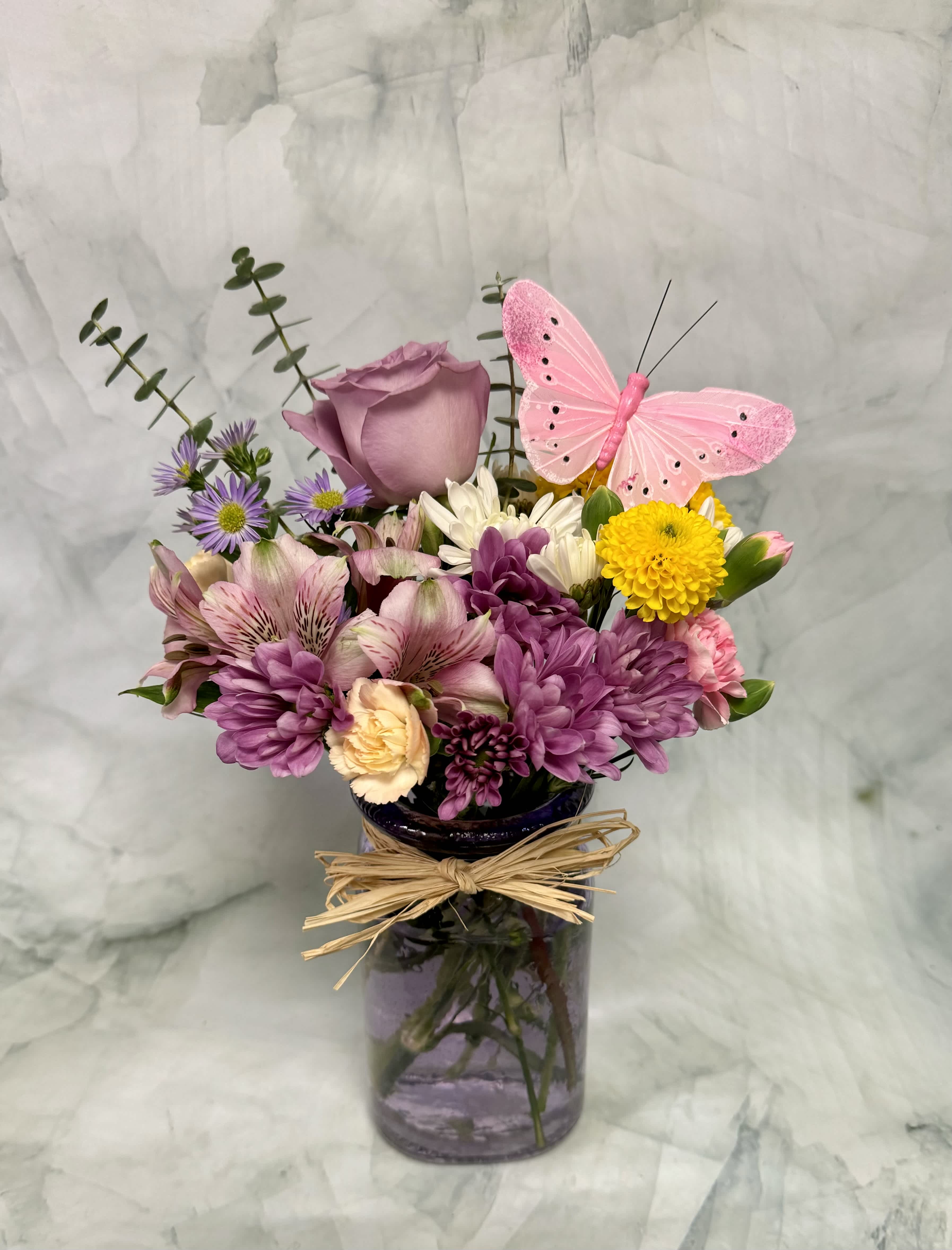 Purple and pink mixed bouquet in a glass vase with a pink butterfly pick