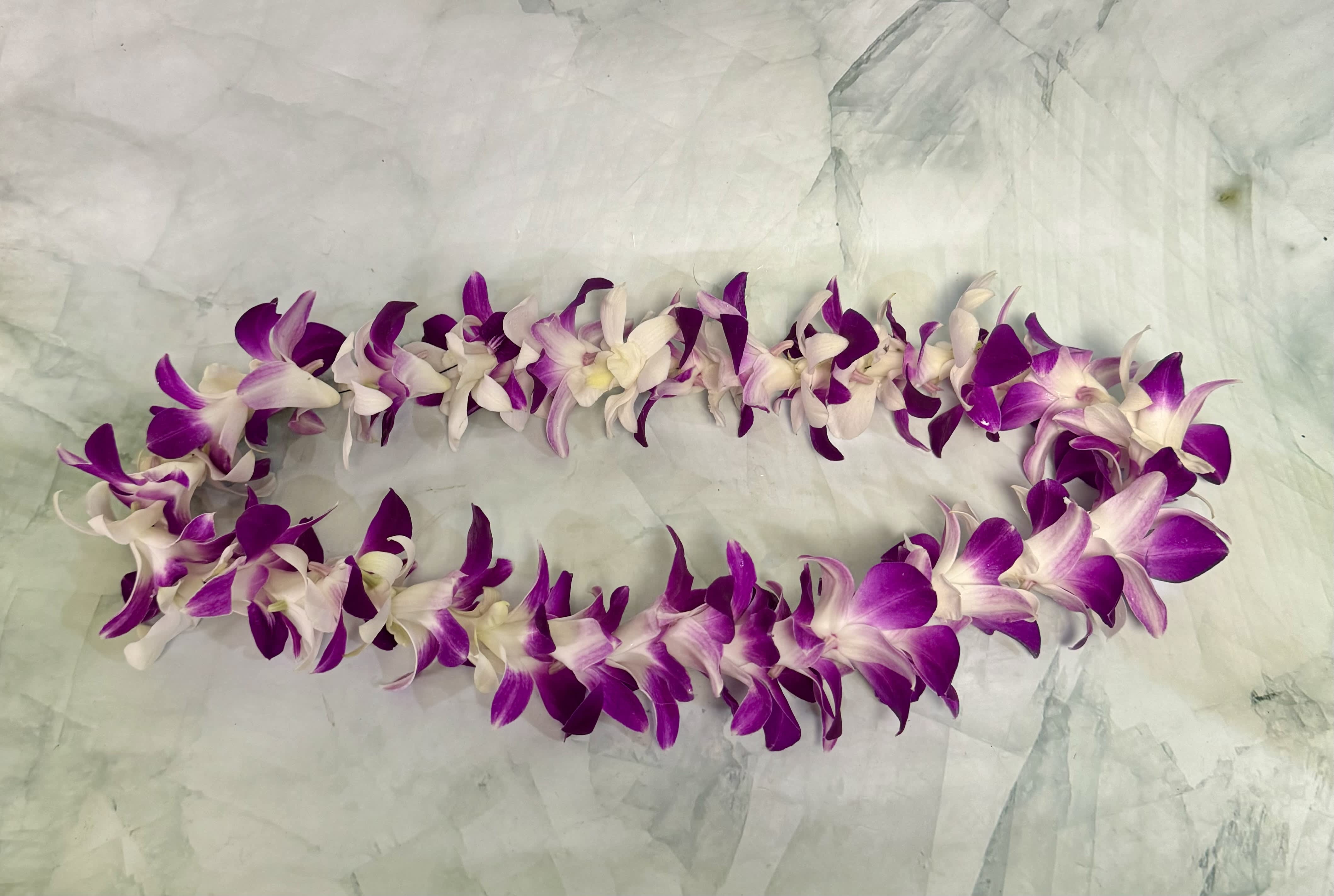 Purple and white orchid lei on a pale fabric background