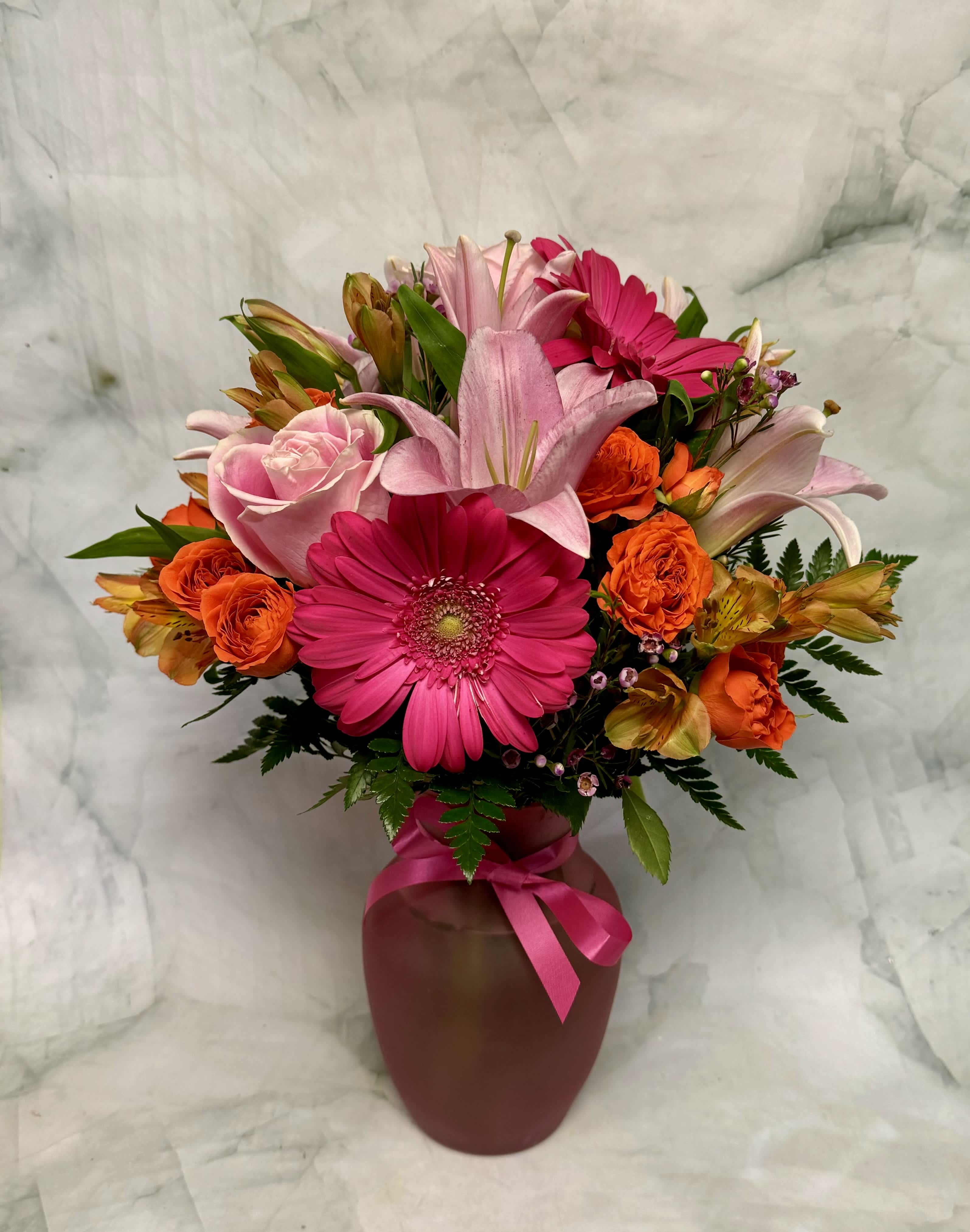 Pink and orange mixed flower arrangement in a vase with a ribbon