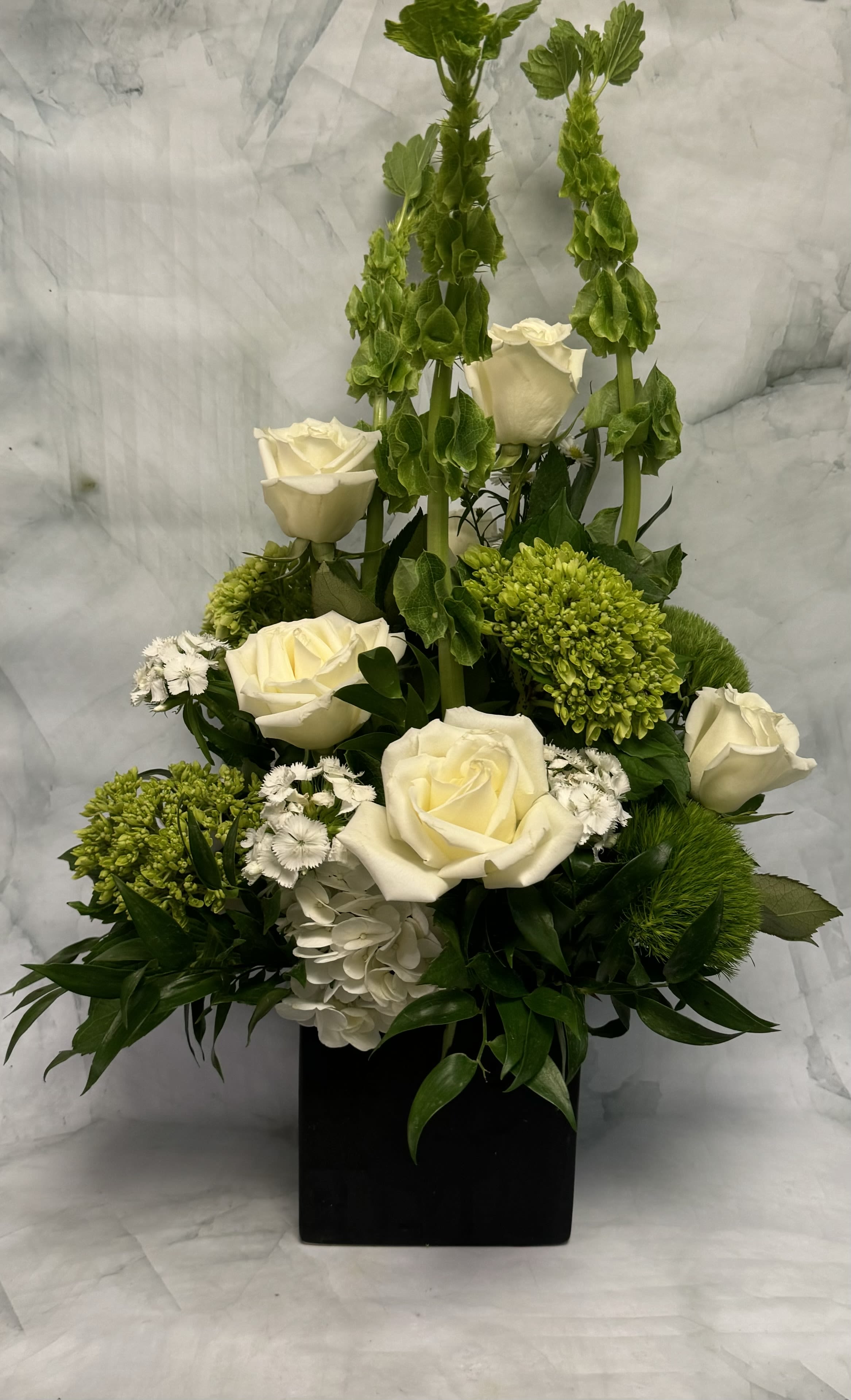 White roses and green blooms arranged in a black square vase