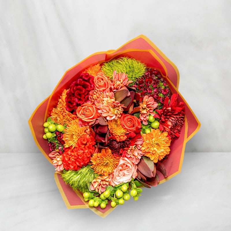 Bright mixed bouquet with orange, red, and pink flowers wrapped in paper