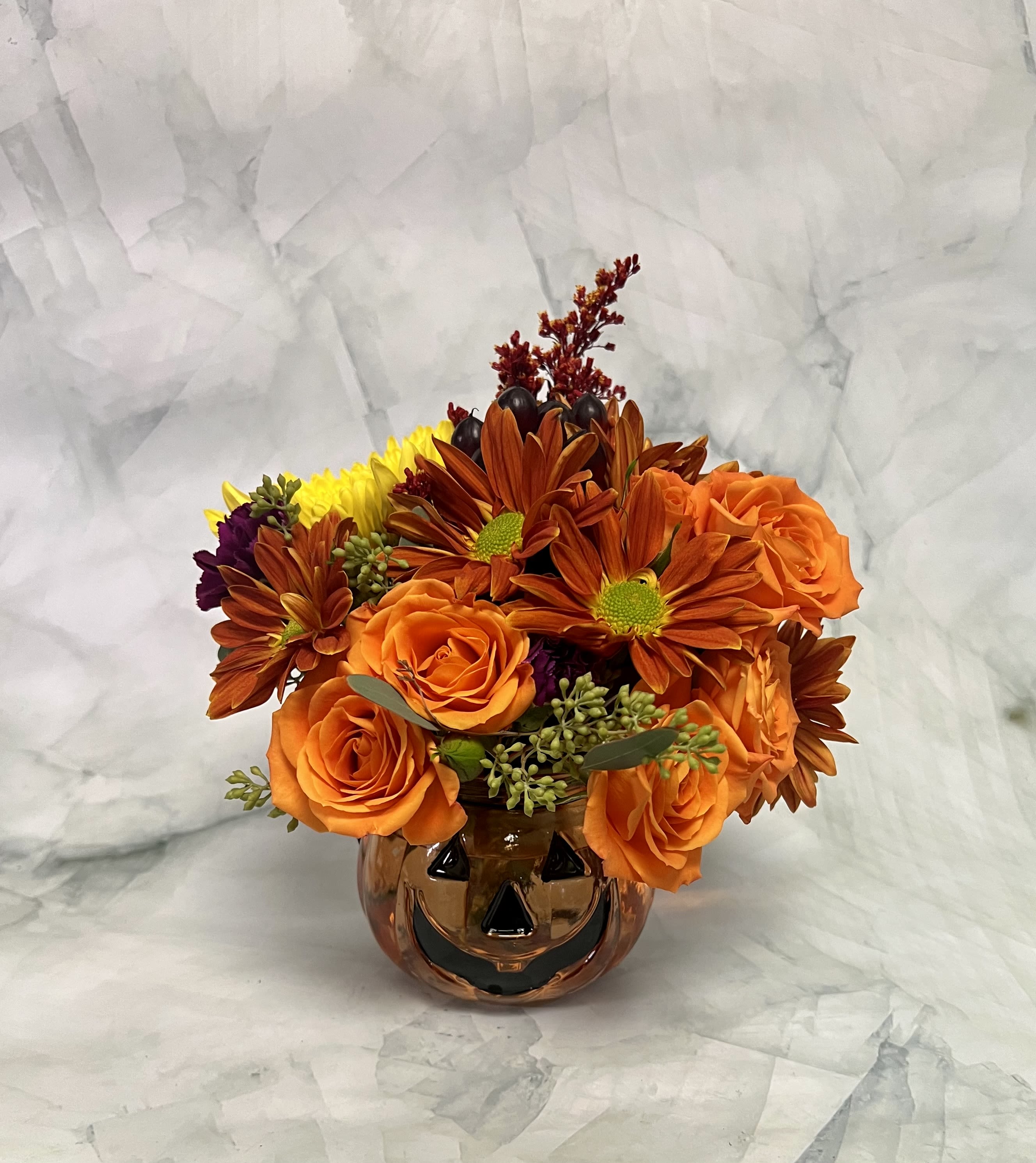 Orange roses and autumn-toned daisies in a pumpkin-shaped vase