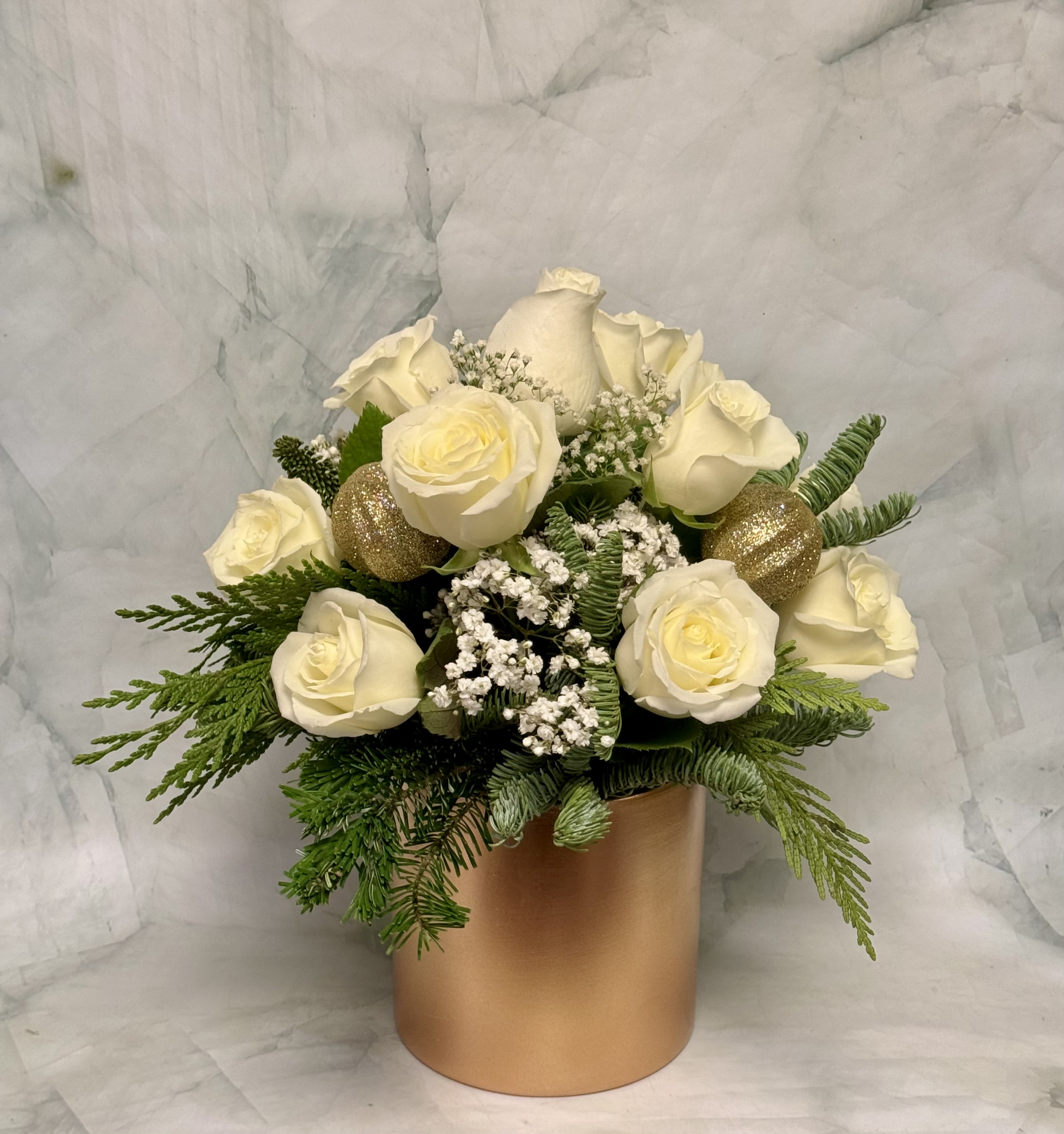 White roses arranged in a gold cylindrical vase with evergreen accents