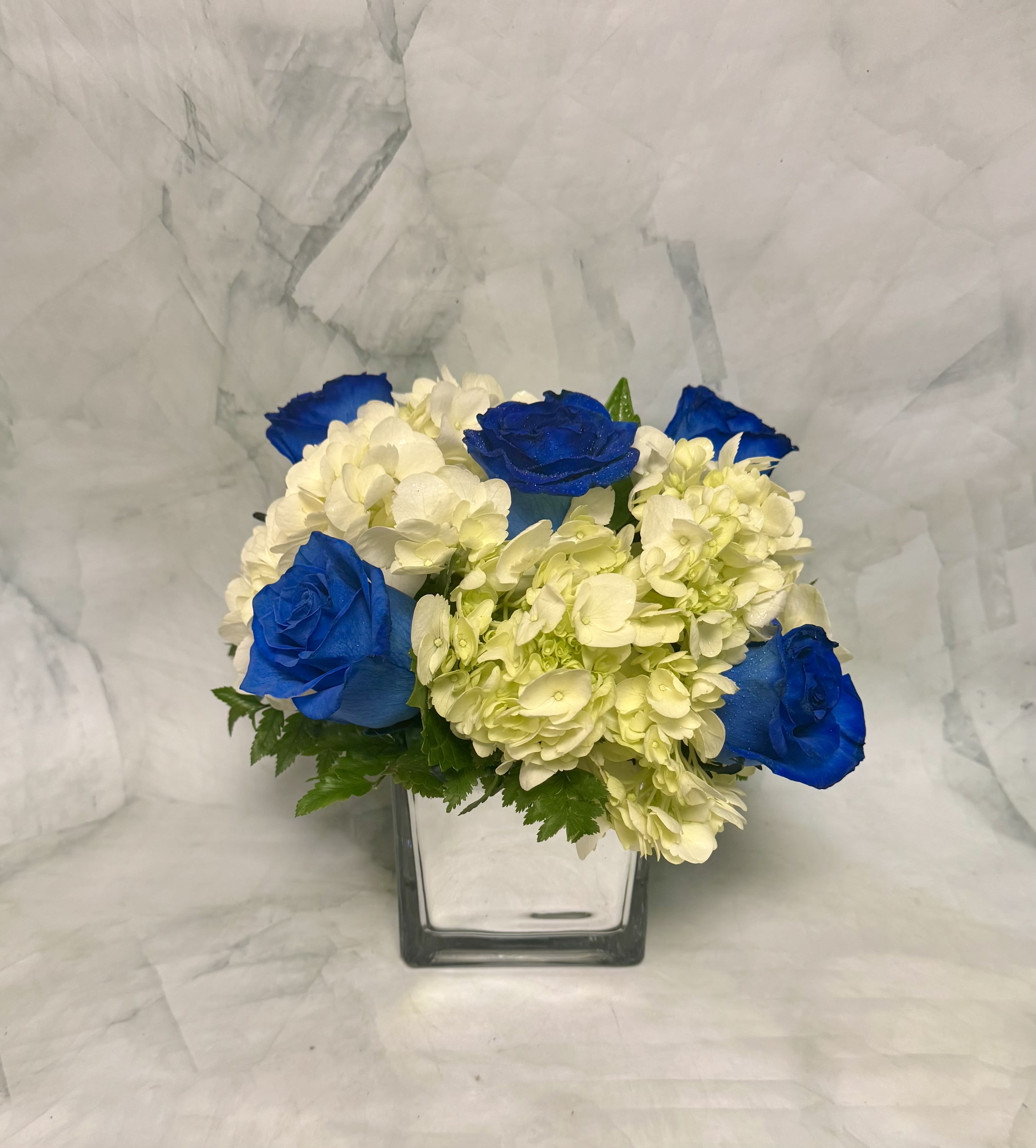 Blue roses and white hydrangeas in a square glass vase
