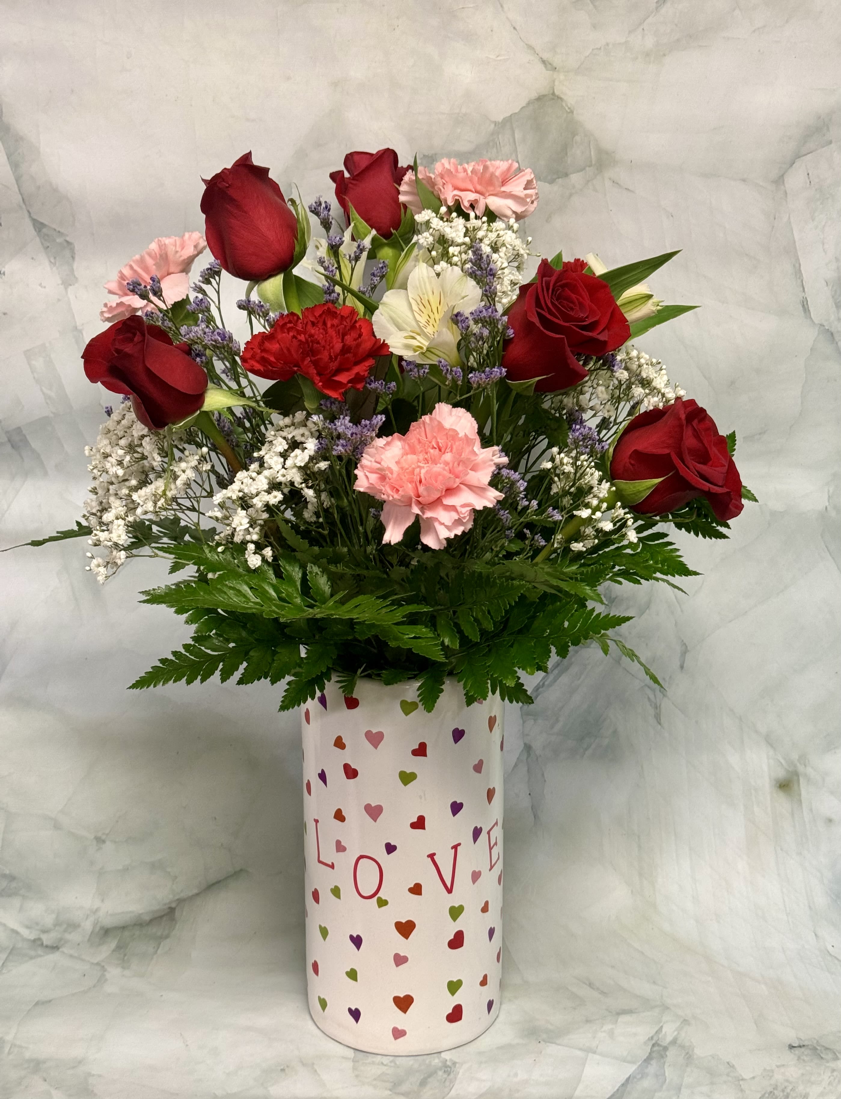 Bouquet of red roses and pink carnations in a heart-patterned vase