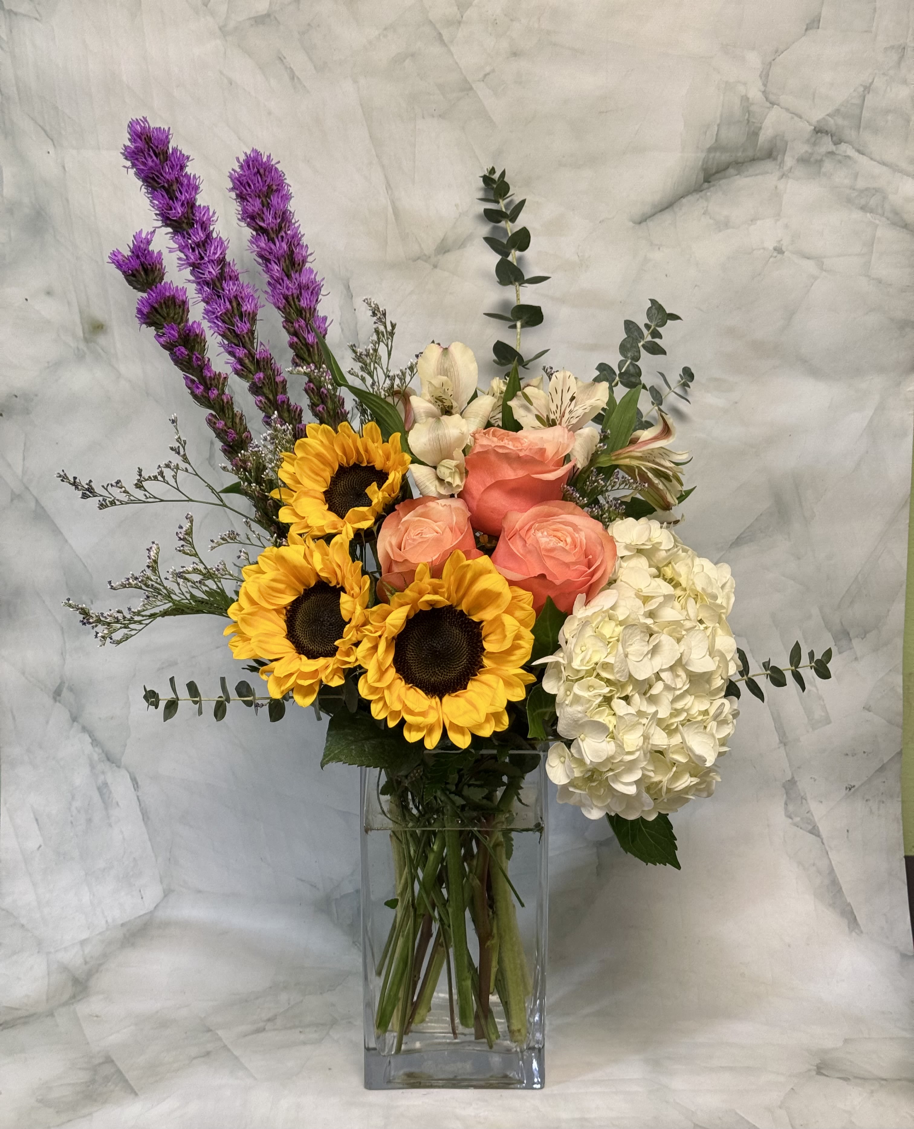 Bouquet of sunflowers, roses, and hydrangea in a glass vase