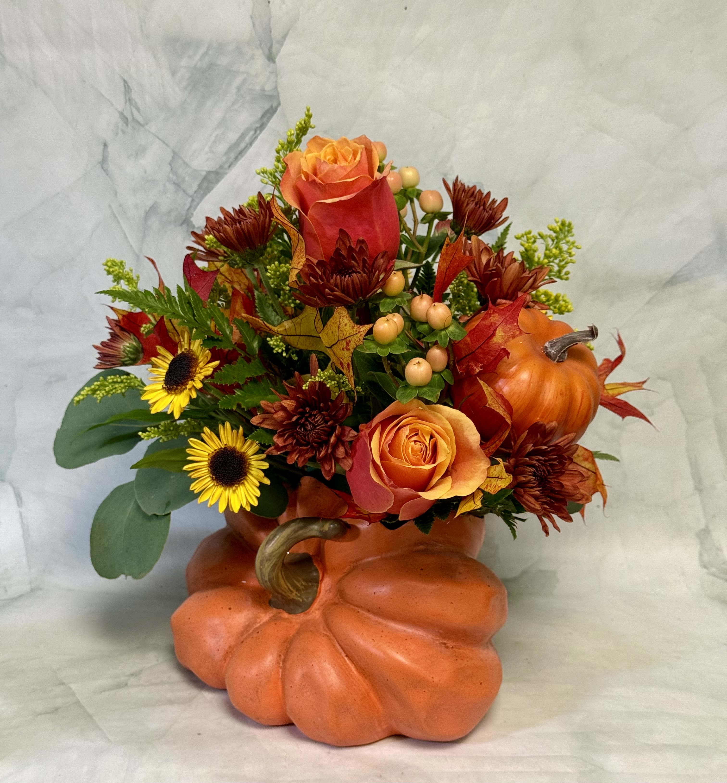 Fall floral arrangement in a pumpkin-shaped container with orange roses and sunflowers