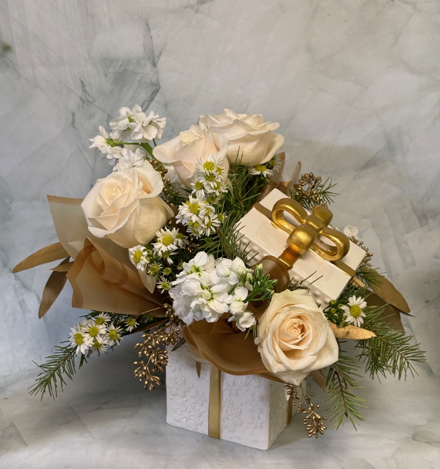 Cream roses and small white flowers arranged with a gift box and gold ribbon