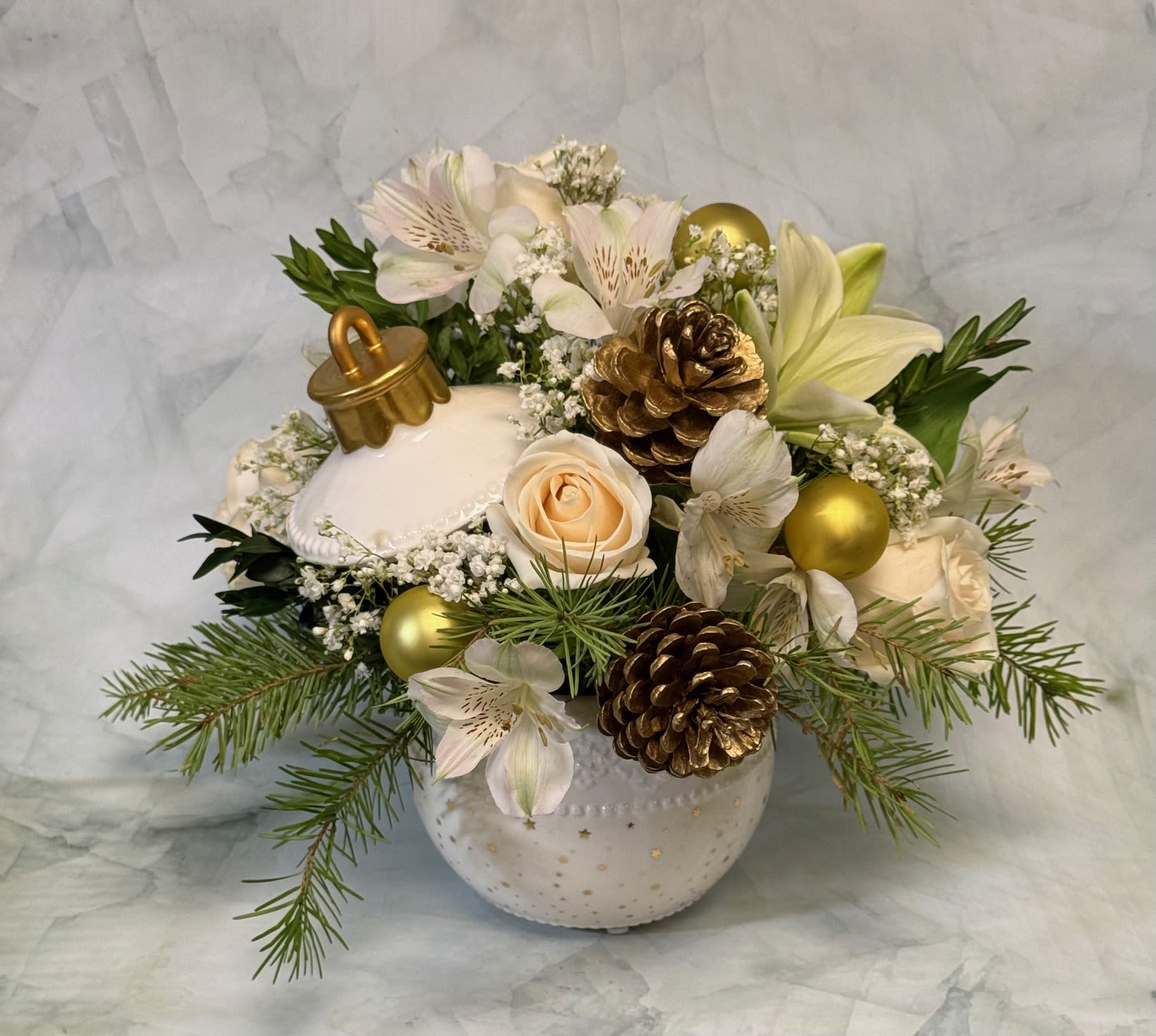 White floral arrangement with lilies, roses, pinecones, and gold ornaments in a ceramic vase