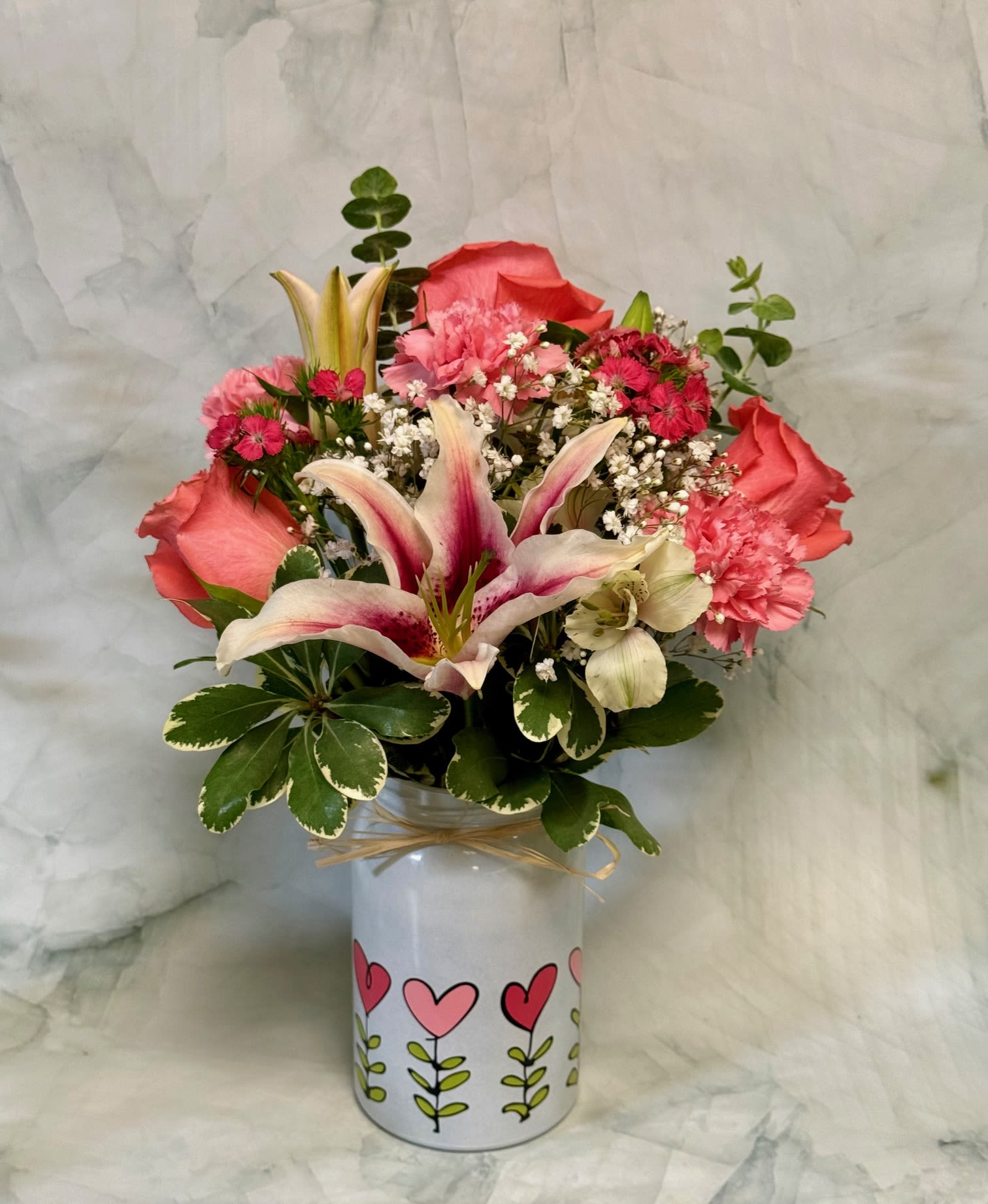 Pink lilies, roses, and carnations arranged in a white vase with heart designs