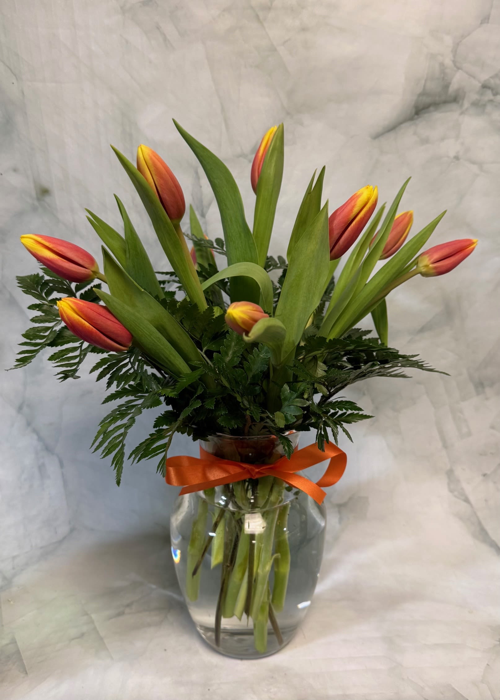 Orange and yellow tulips arranged in a clear glass vase with a ribbon.