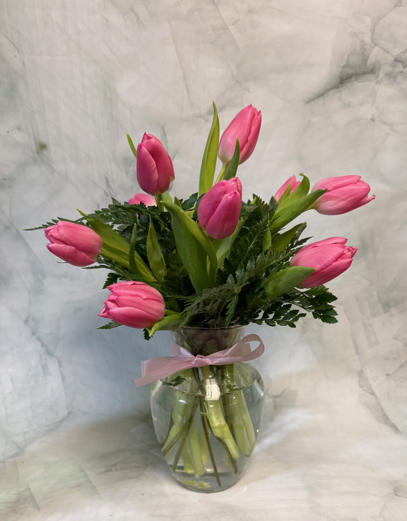 Pink tulip bouquet in a clear glass vase with a pink ribbon