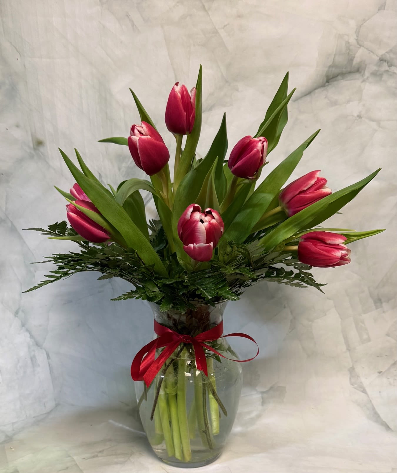 Pink tulips arranged in a clear glass vase with a red ribbon