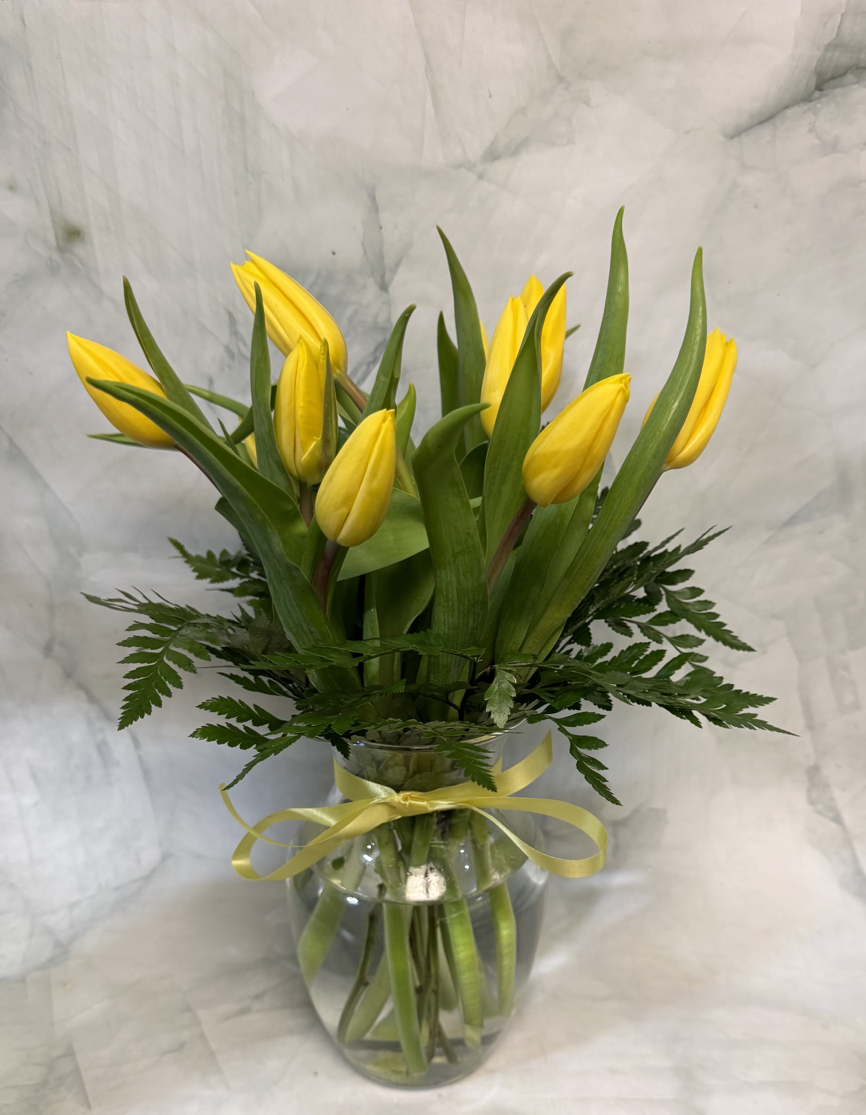 Yellow tulip bouquet in a glass vase with a yellow ribbon