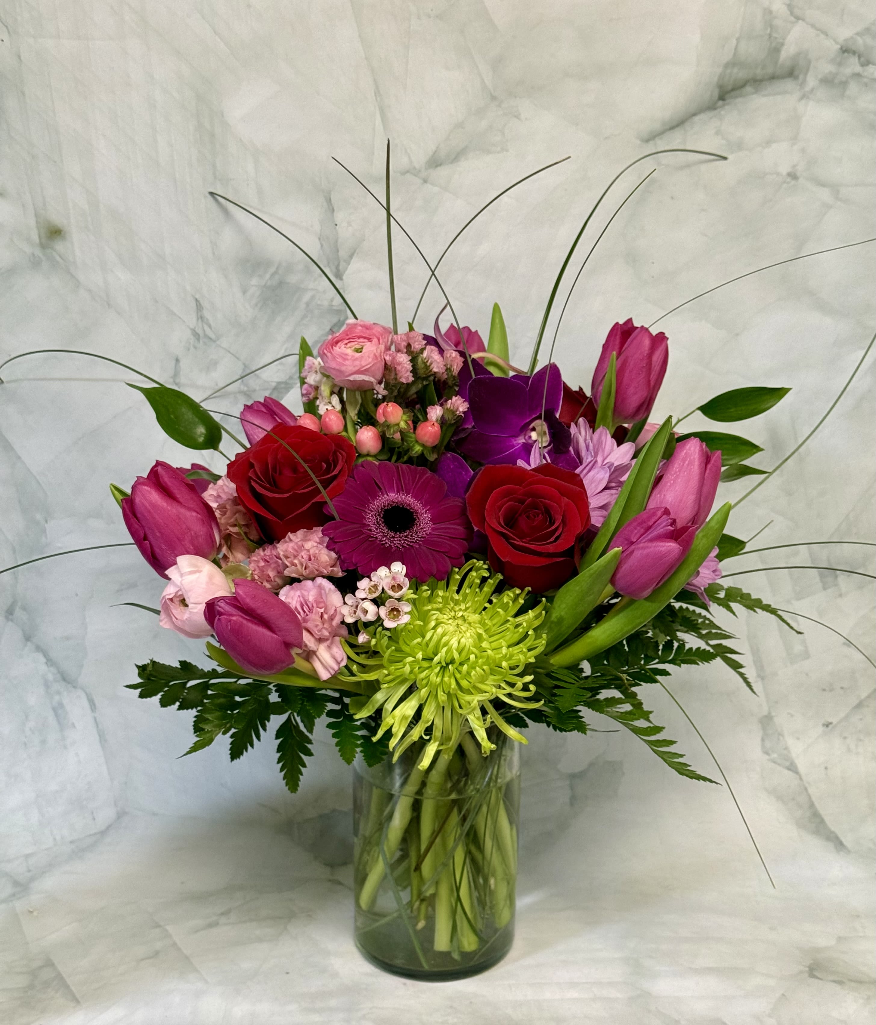 Mixed bouquet of pink, red, and purple flowers in a glass vase