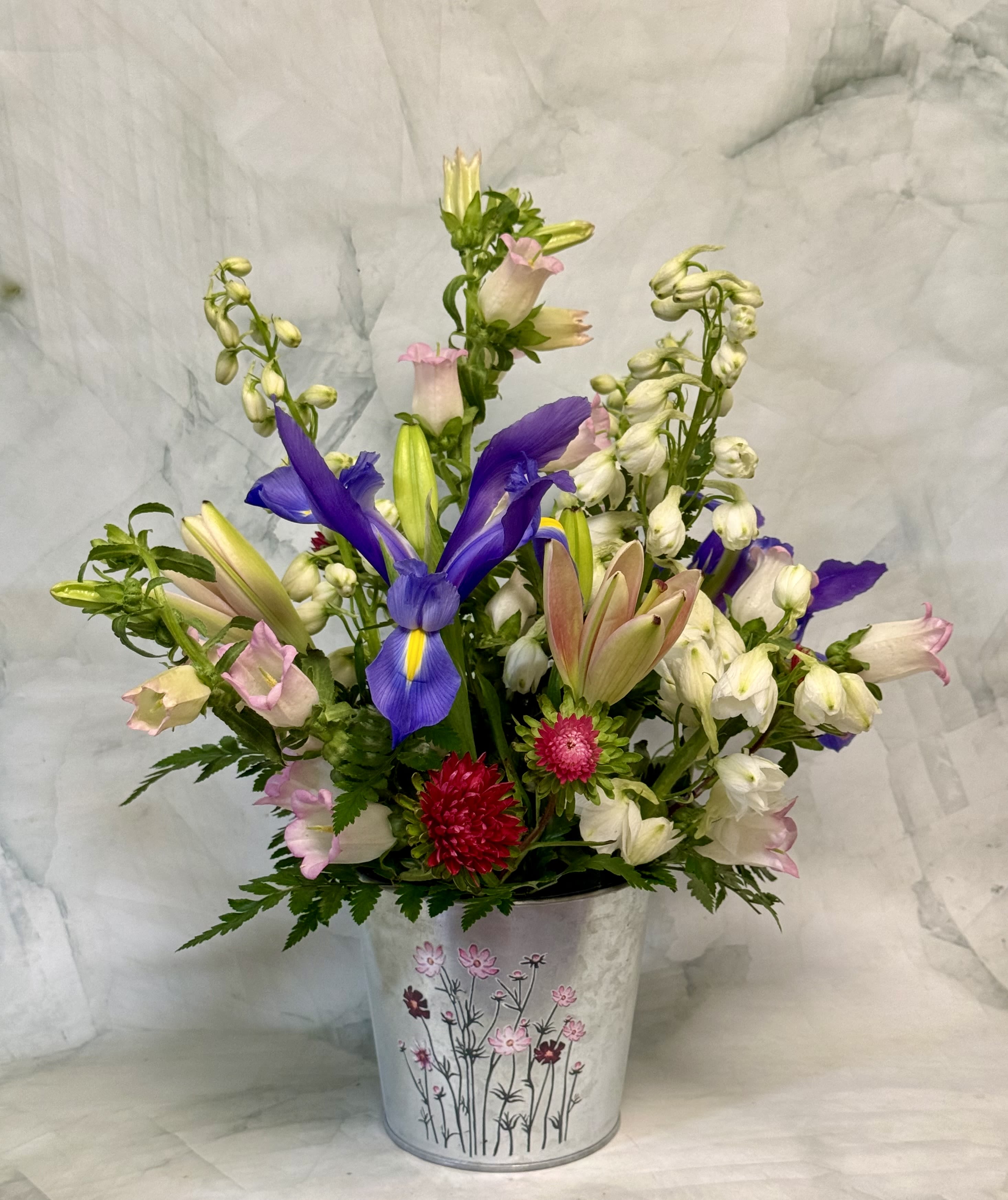 Mixed bouquet with purple irises and pink-white blooms in a decorative metal bucket