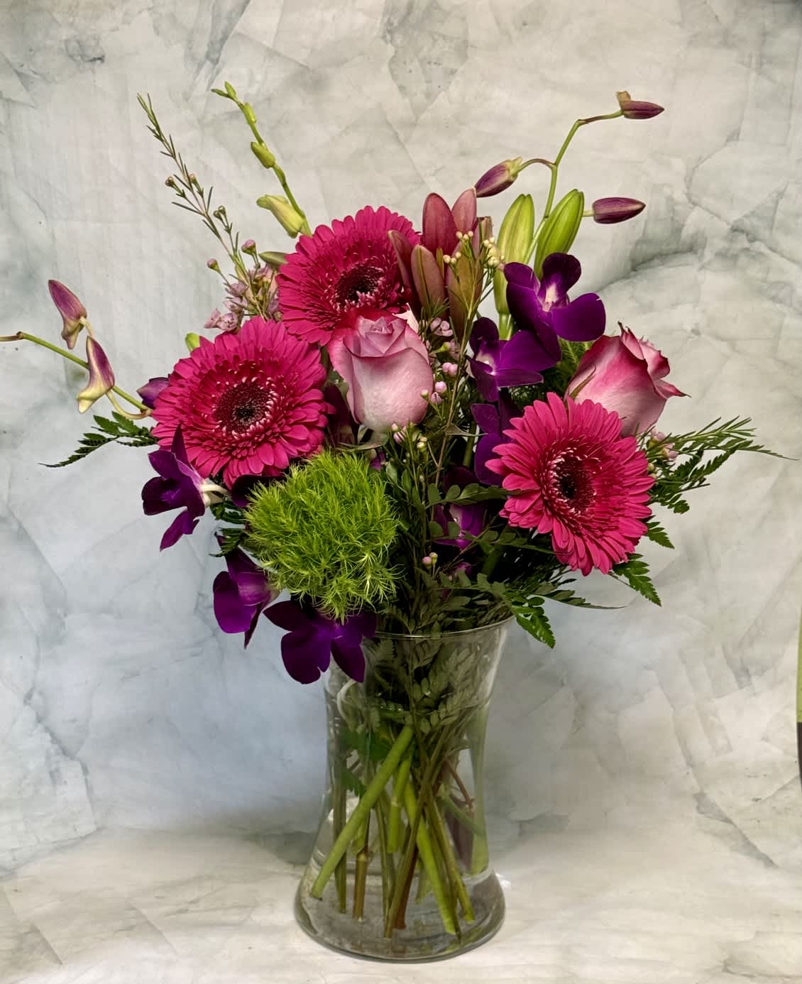 Pink gerberas, roses, and purple orchids in a clear glass vase