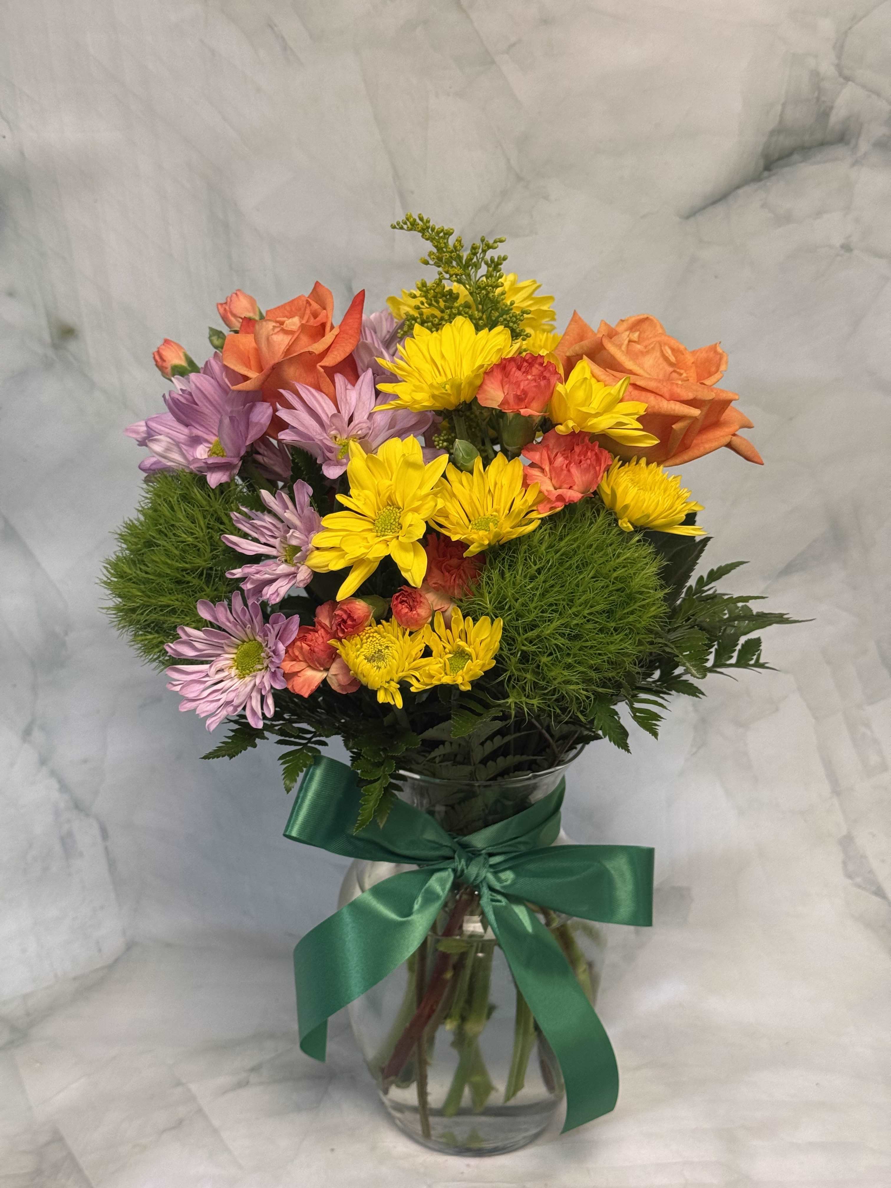 Mixed bouquet of orange roses, yellow daisies, and purple flowers in a glass vase