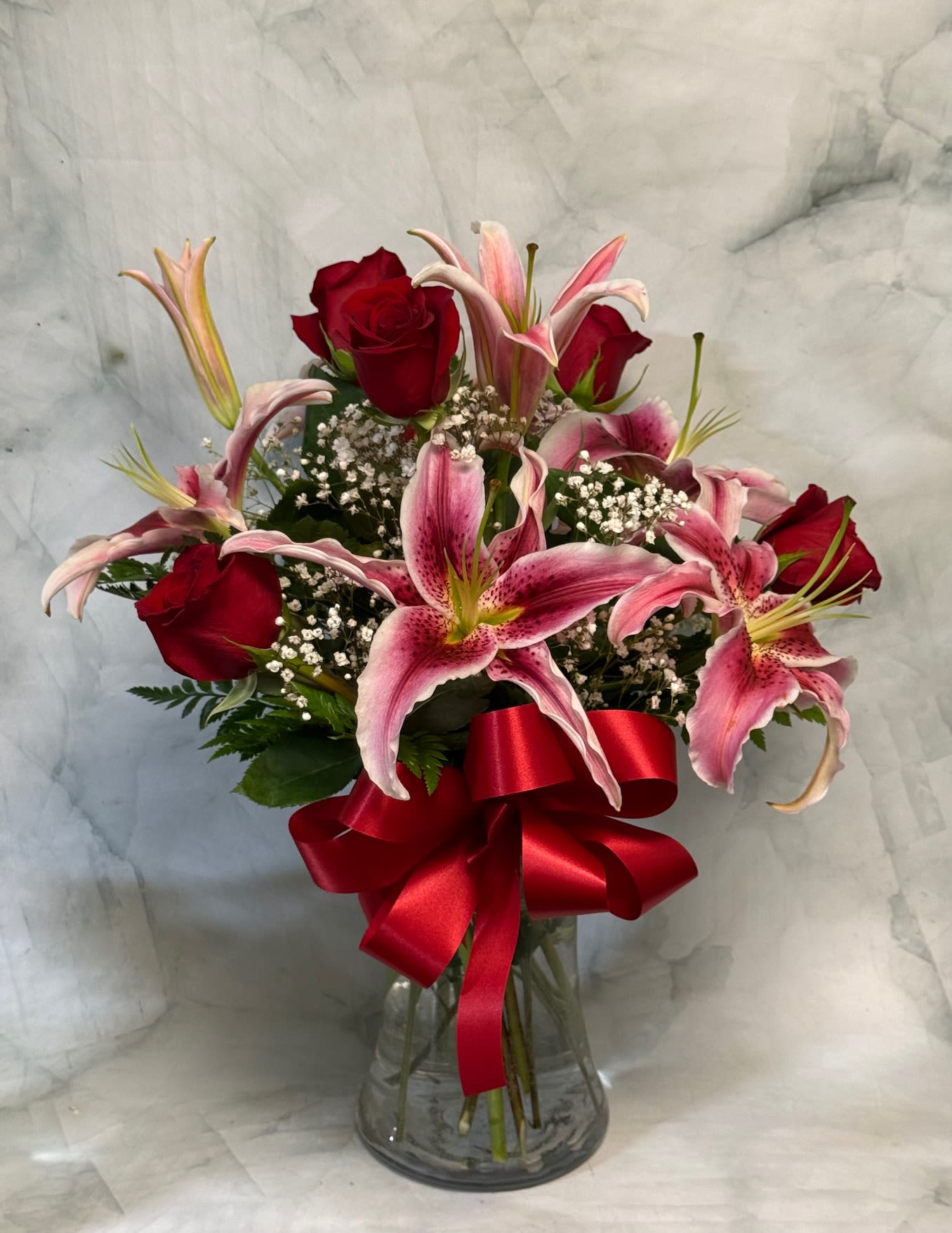 Red roses and pink lilies in a glass vase with a red ribbon
