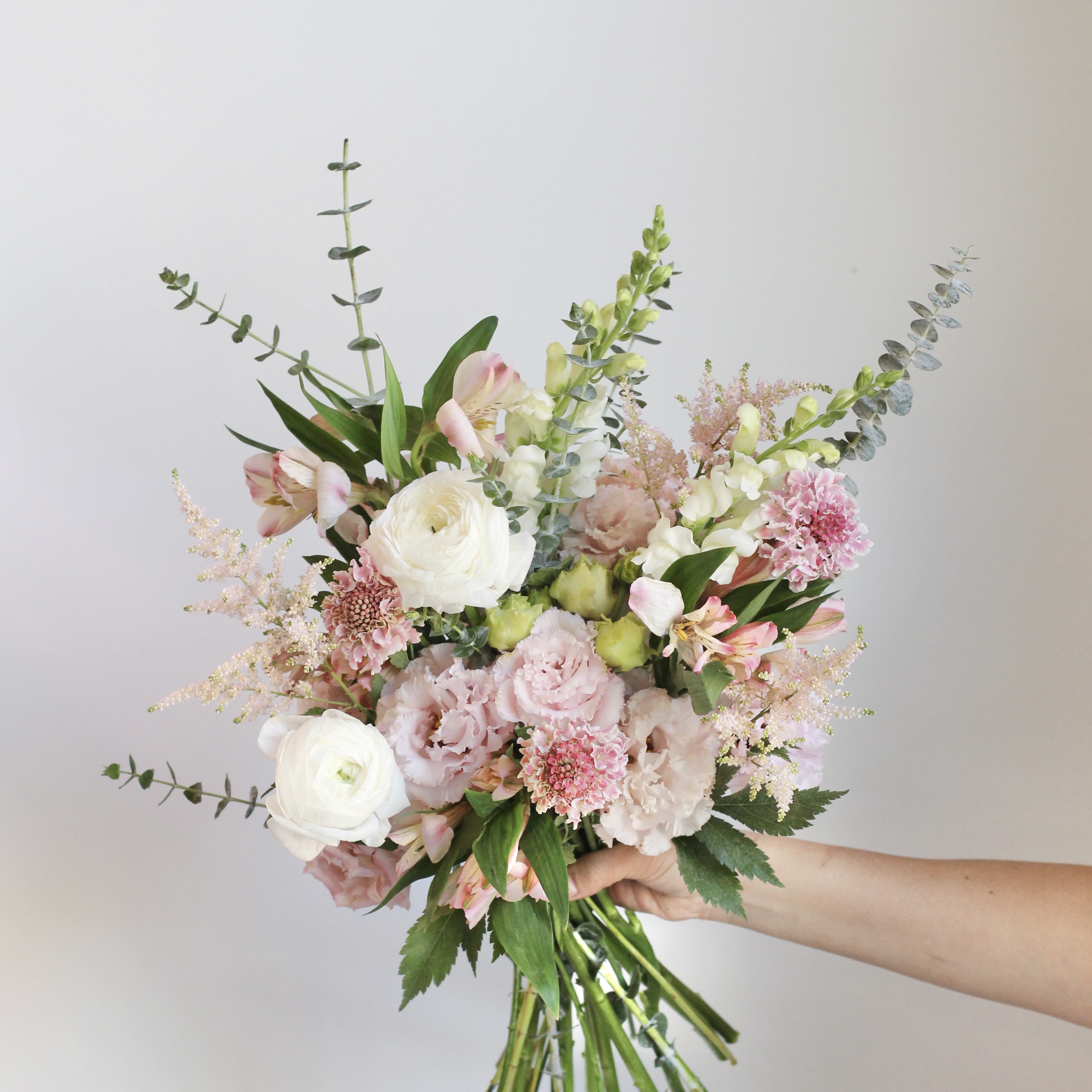 Handheld bouquet of pink and white flowers with long eucalyptus stems