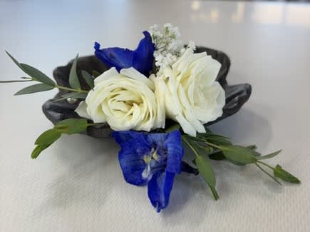 Small floral corsage with white roses and blue flowers on a dark base