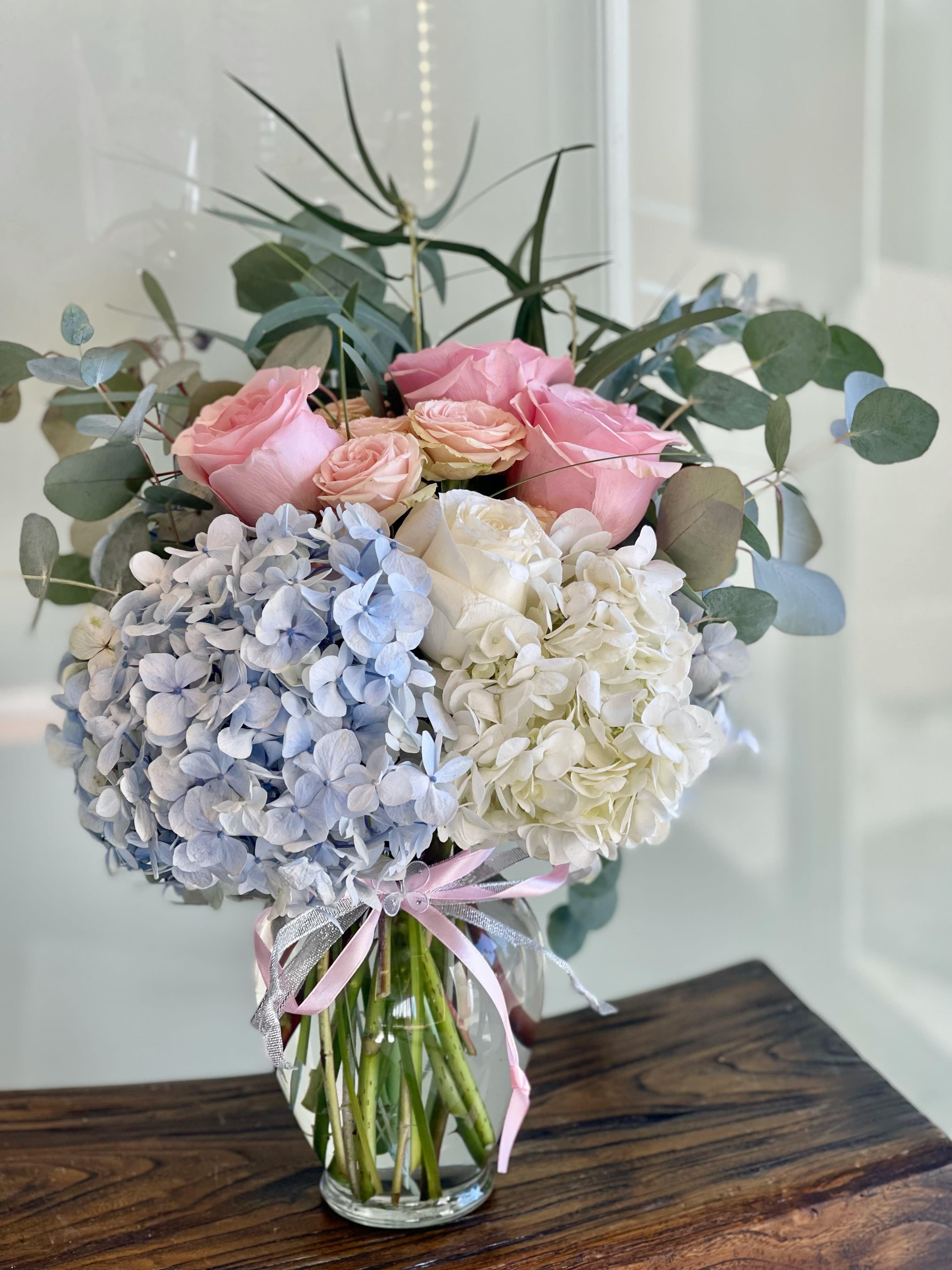 Pink roses and blue-white hydrangeas in a glass vase with ribbon