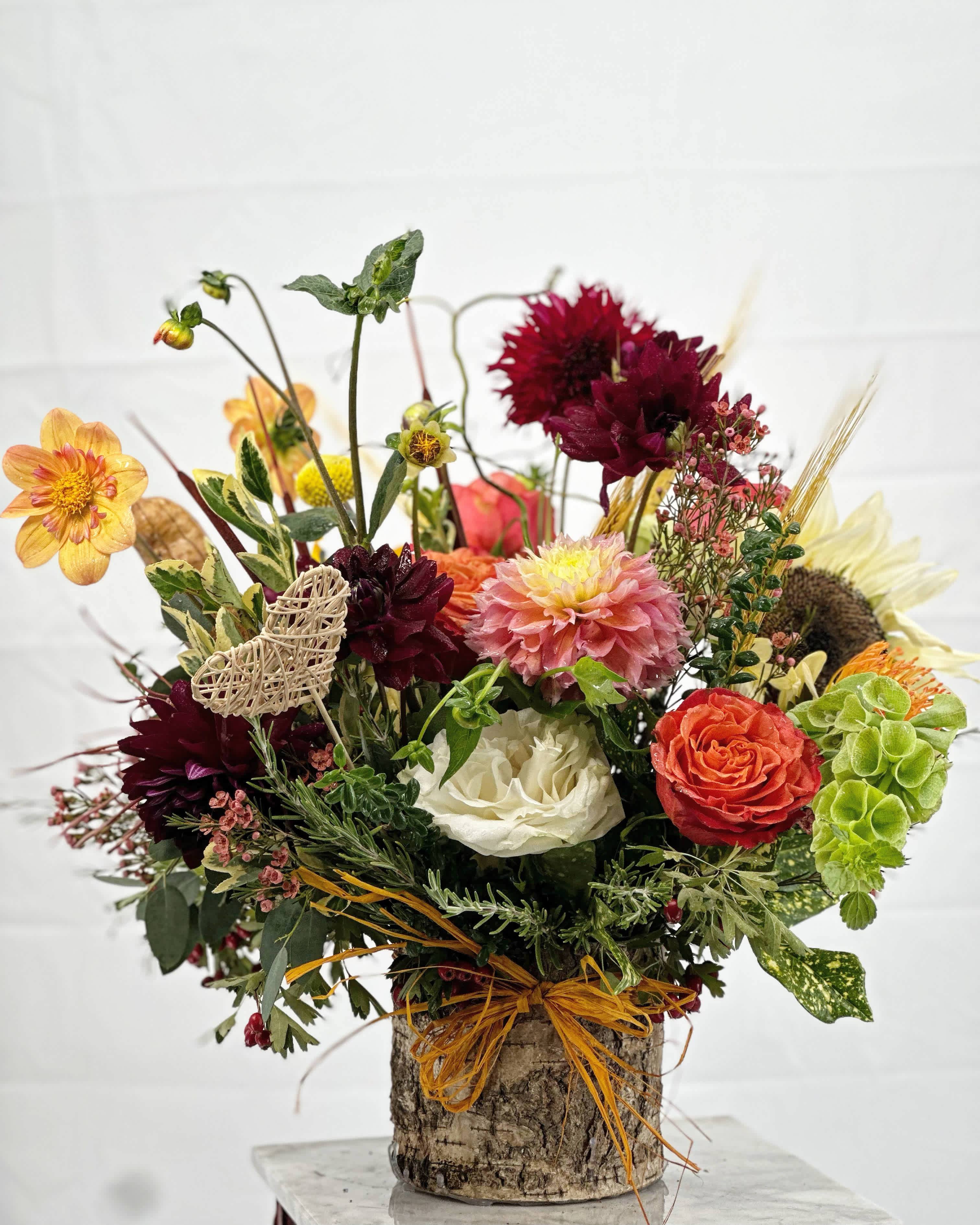 Mixed bouquet in a bark-covered container with burgundy, peach, white, and green flowers