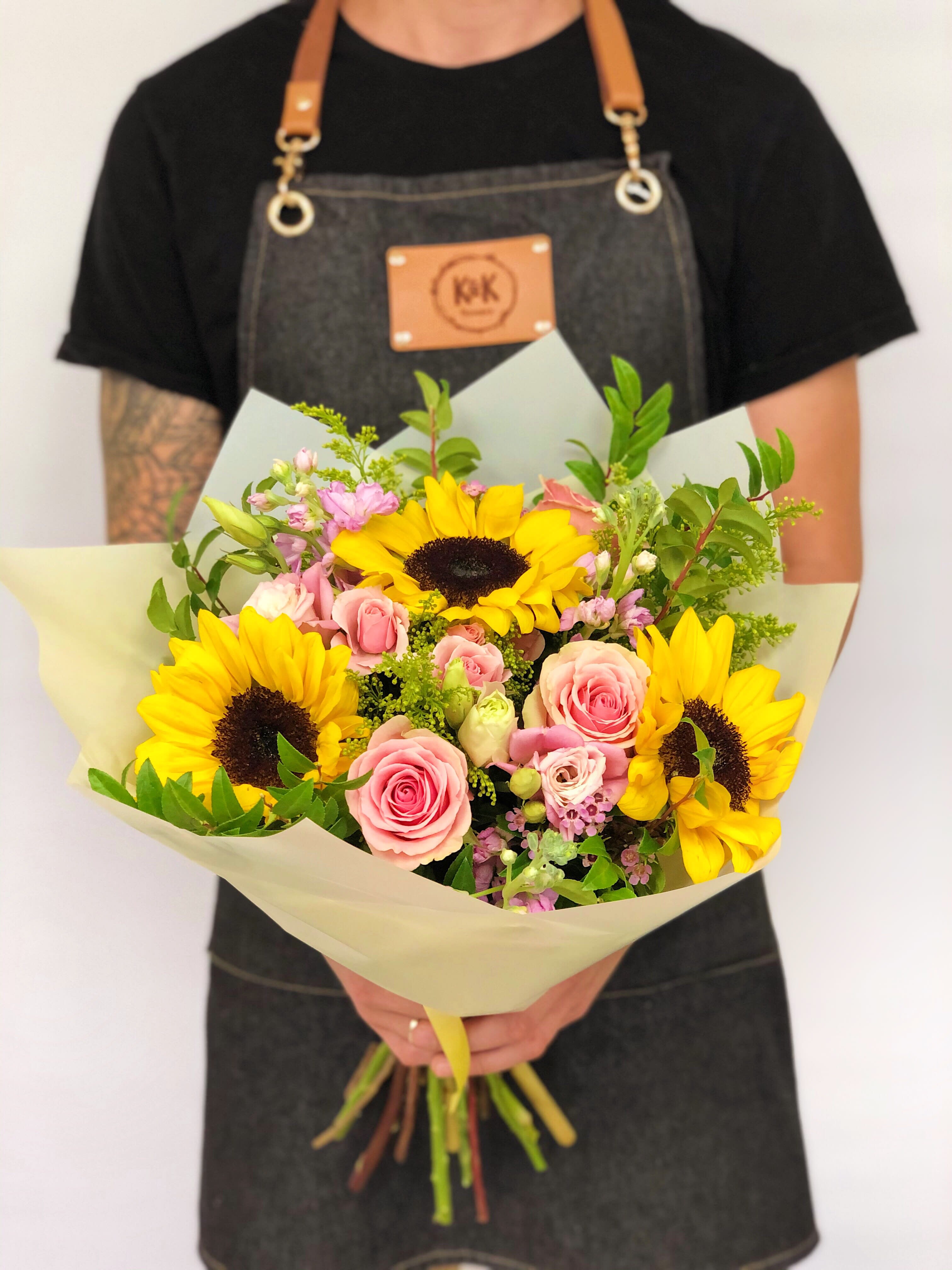Hand-tied bouquet of yellow sunflowers and pink roses wrapped in pale paper