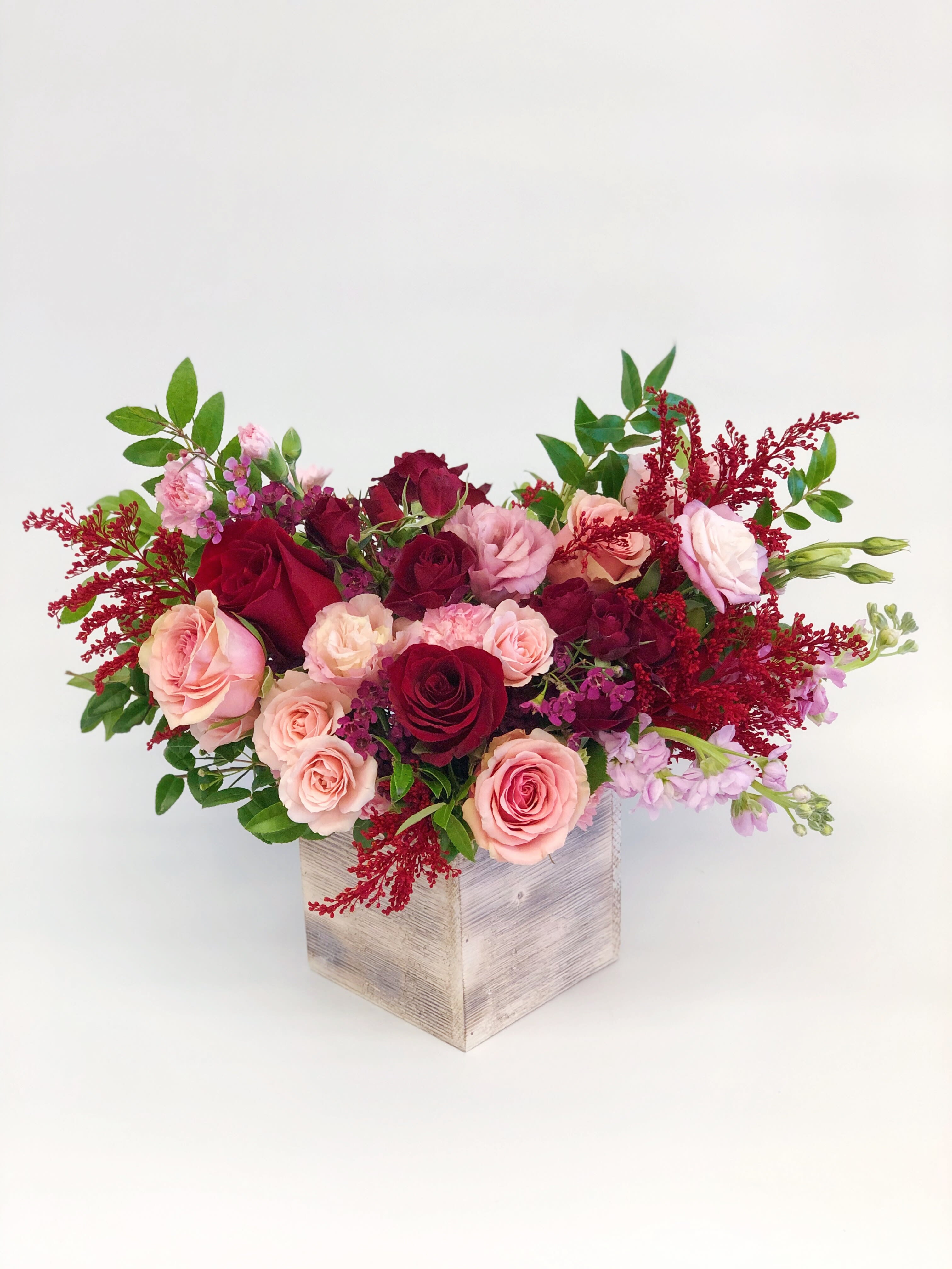 Pink and burgundy roses arranged in a wooden box