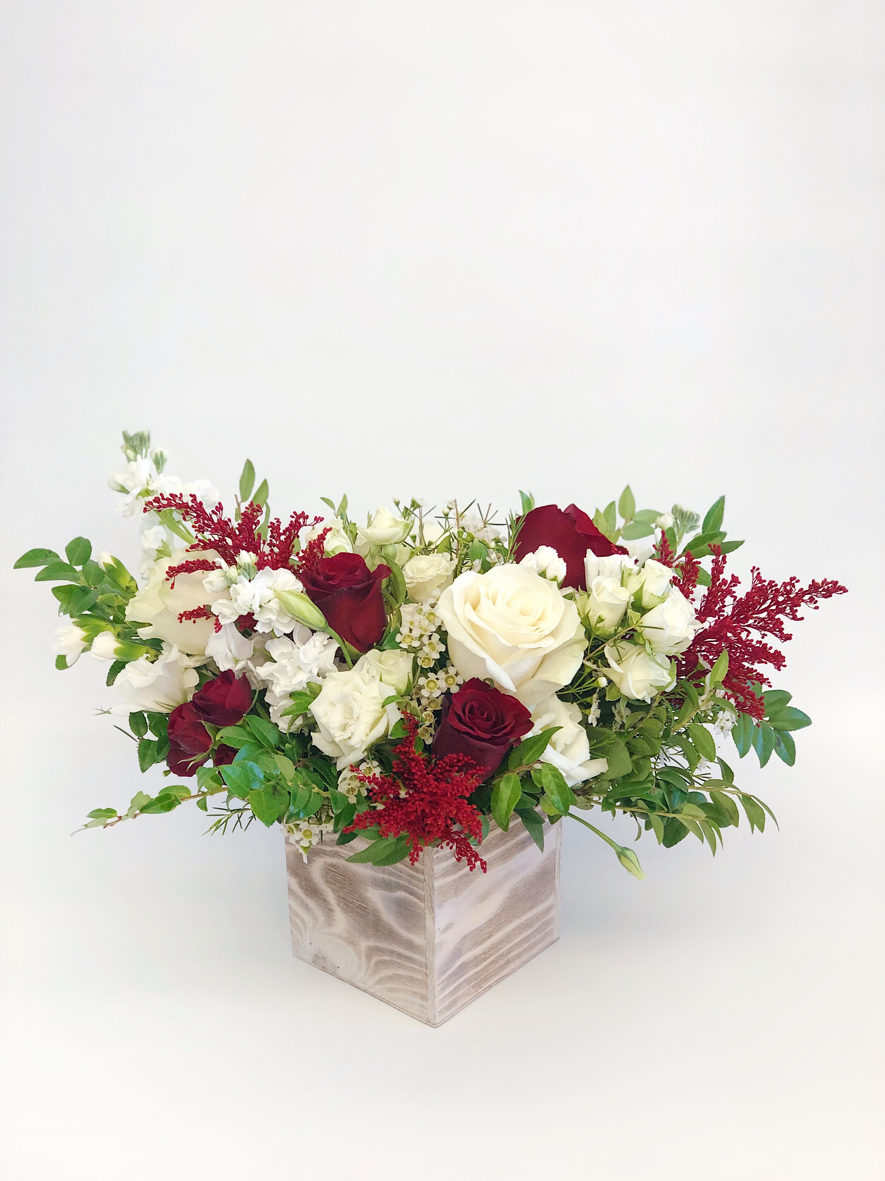 Red and white rose arrangement in a square wooden vase