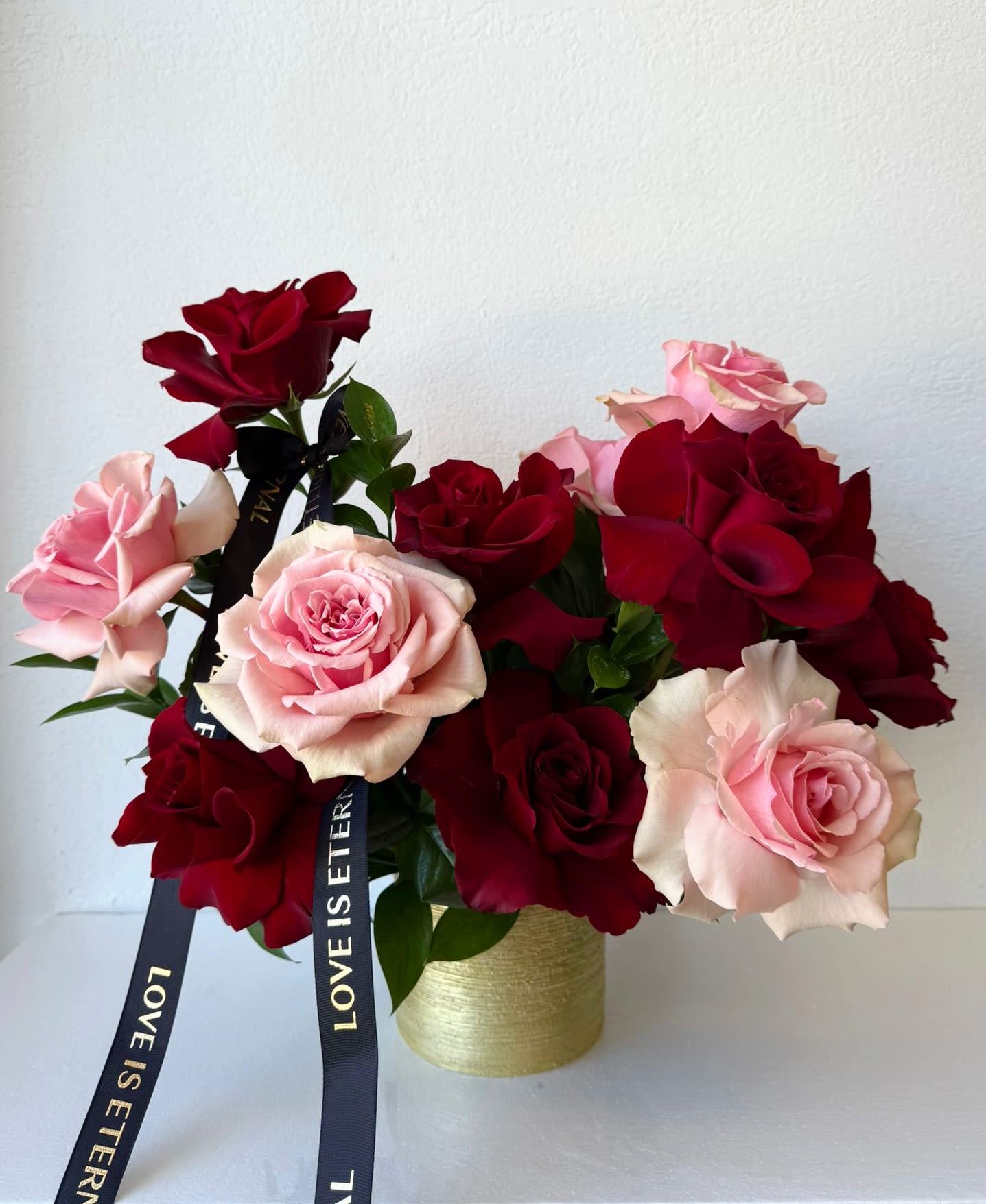 Pink and red roses arranged in a gold vase with black ribbons