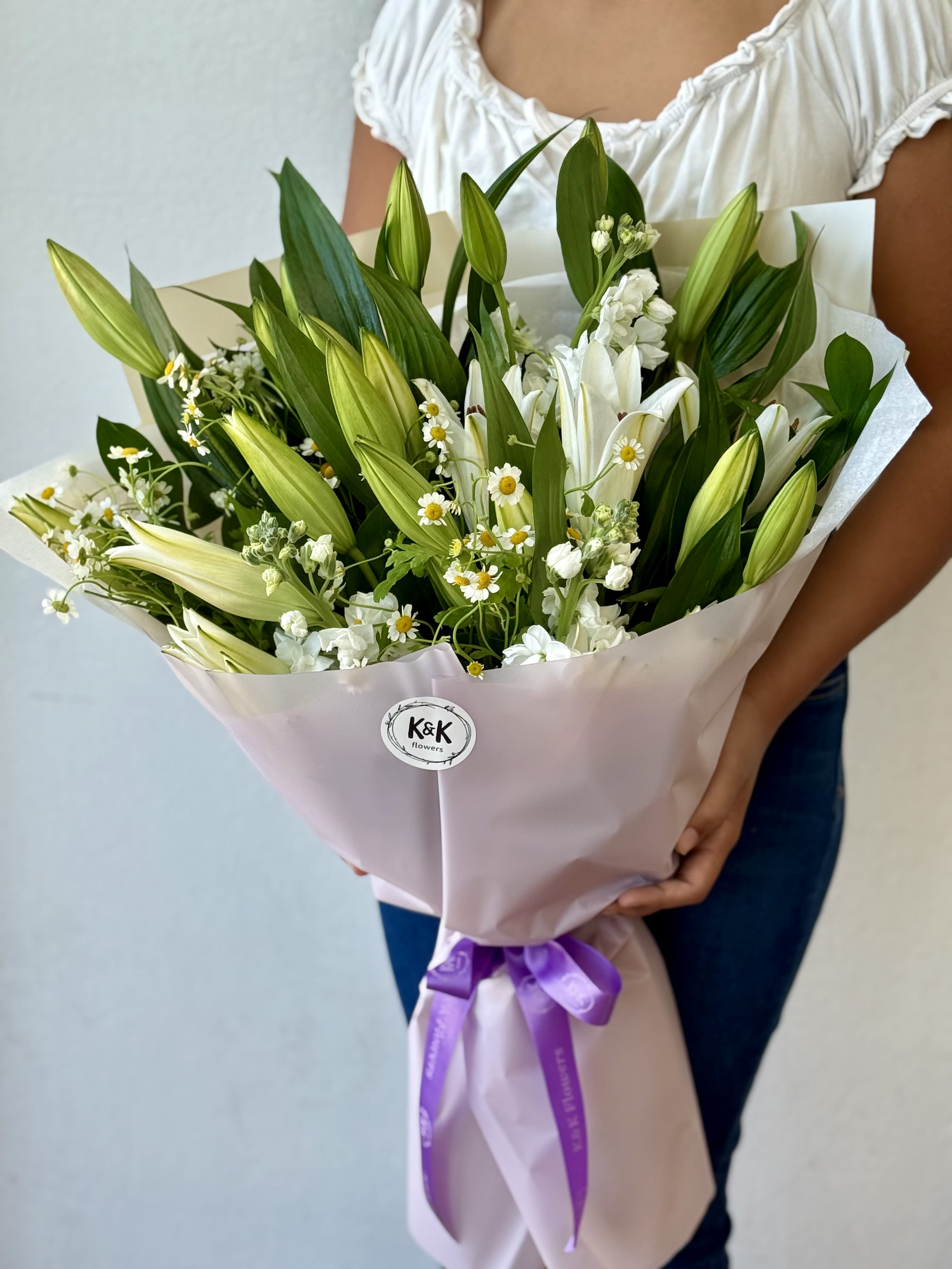 Bouquet of white lilies and small white daisies wrapped in pale pink paper