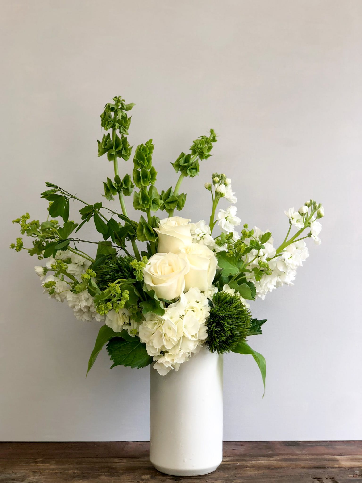 Tall white and green floral arrangement with roses and hydrangeas in a white vase