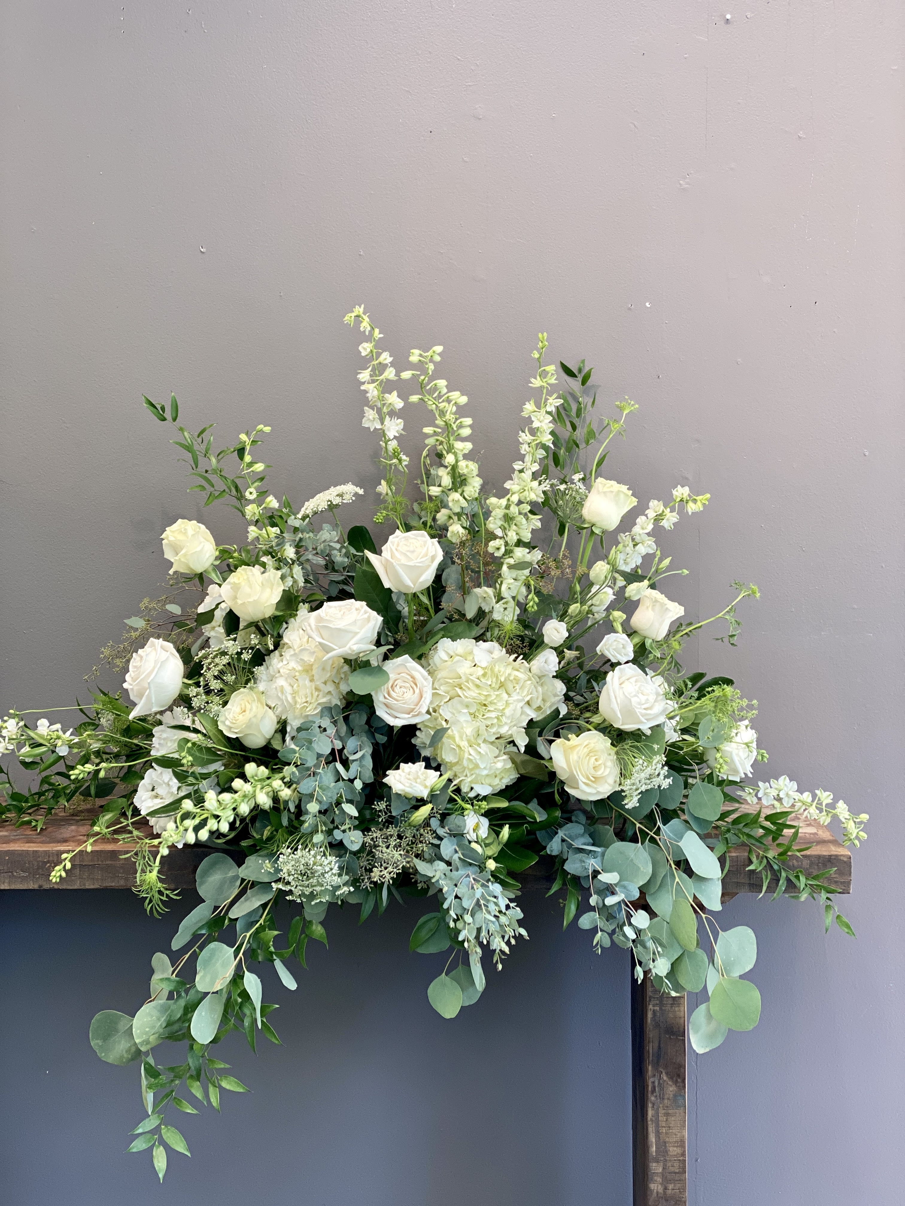 Large white and green floral arrangement with roses and hydrangeas on a wooden stand