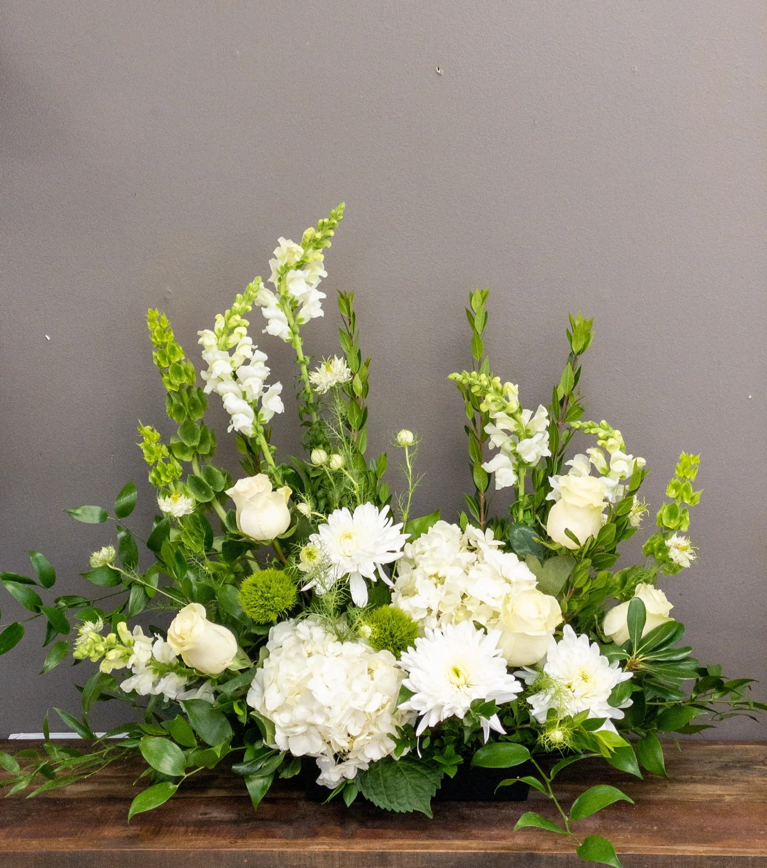 Low white and green floral arrangement with roses, hydrangeas, snapdragons, and mums in a rectangular container