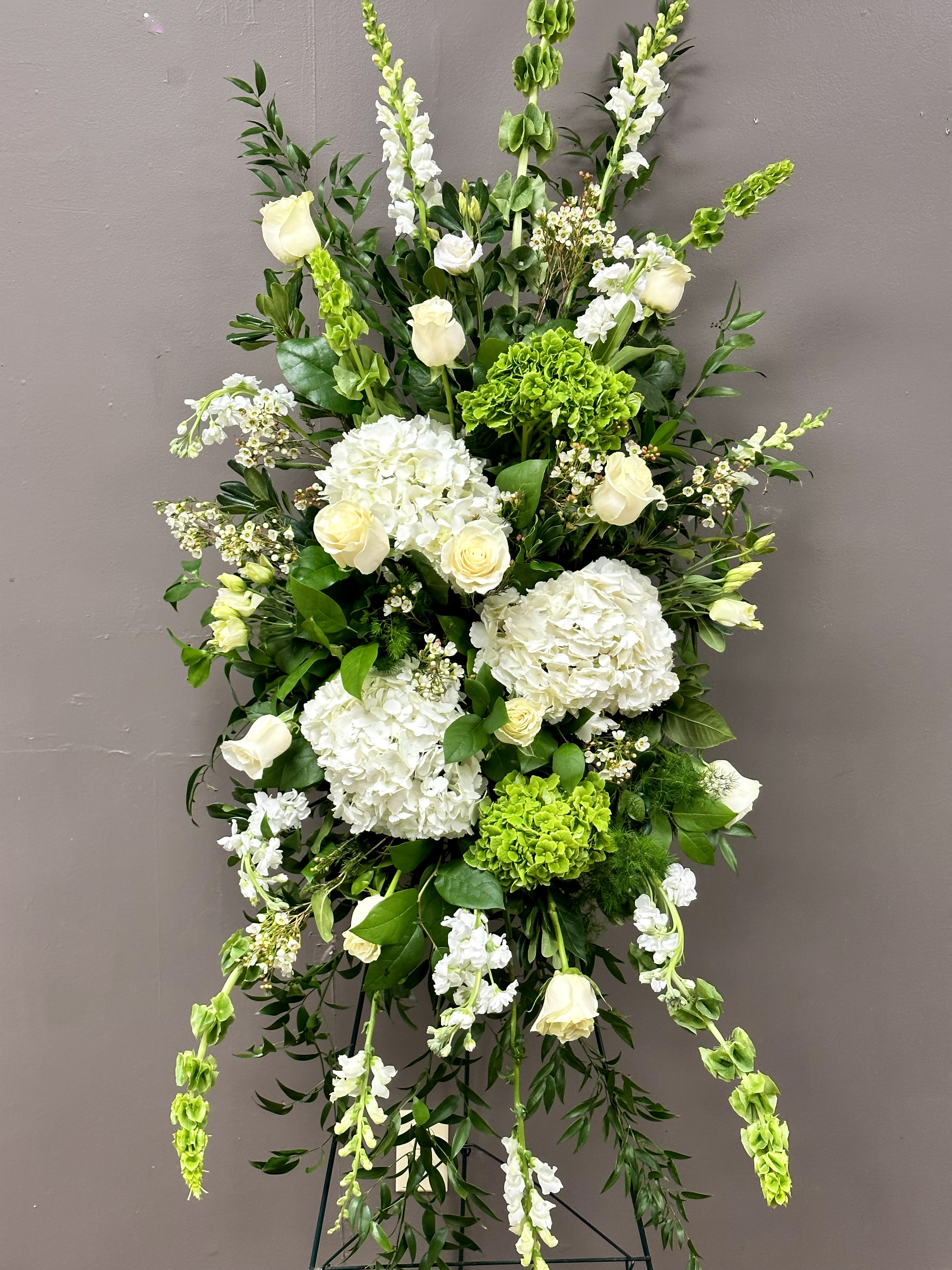 Tall standing spray of white roses and hydrangeas with green accents on an easel stand