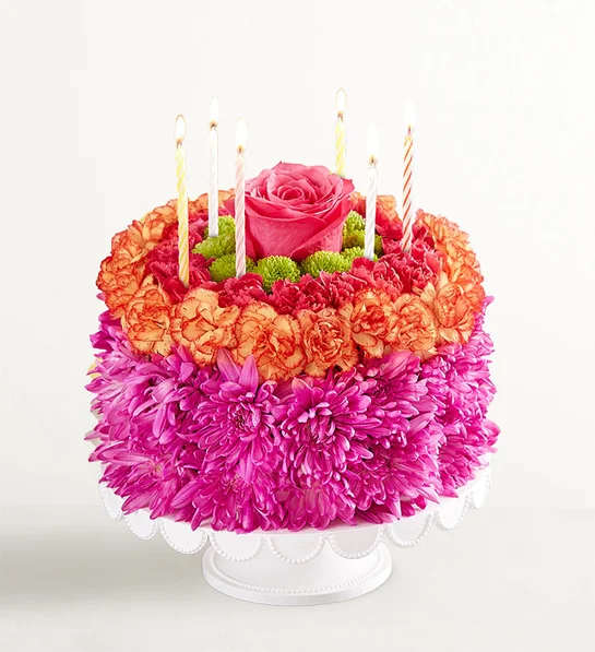 Round flower cake with a pink rose center and striped candles on a white stand