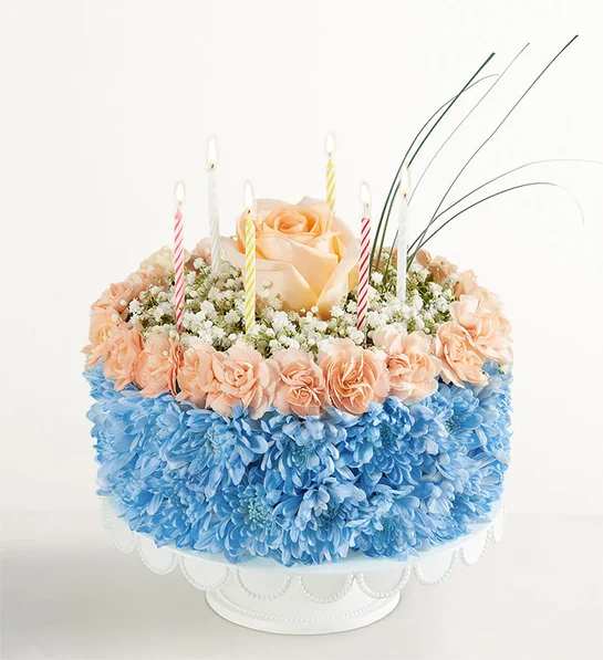 Round floral cake with peach roses, blue flowers, and striped candles