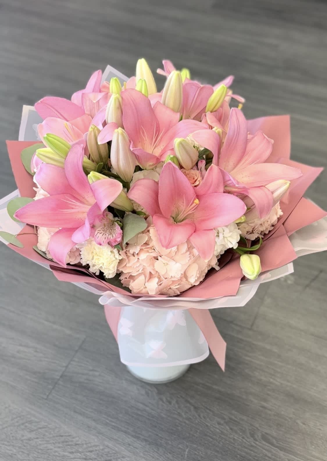 Pink lily bouquet in a white vase with pastel wrapping