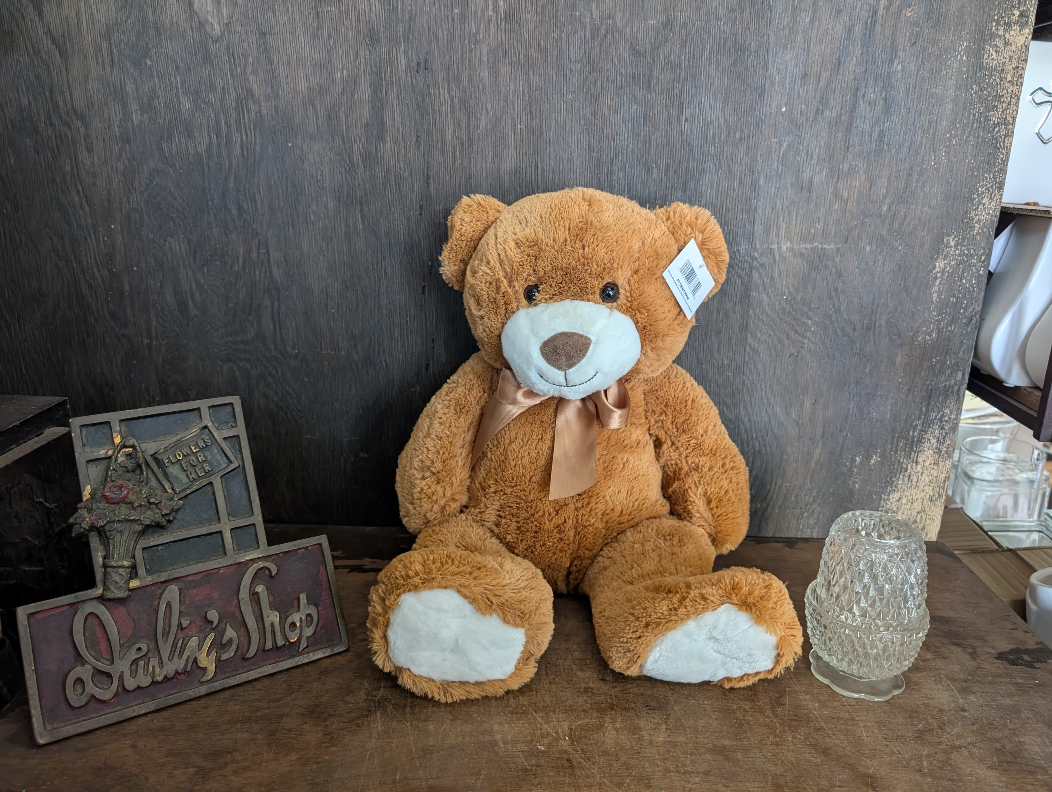 Brown teddy bear with a ribbon sitting beside a glass candle holder