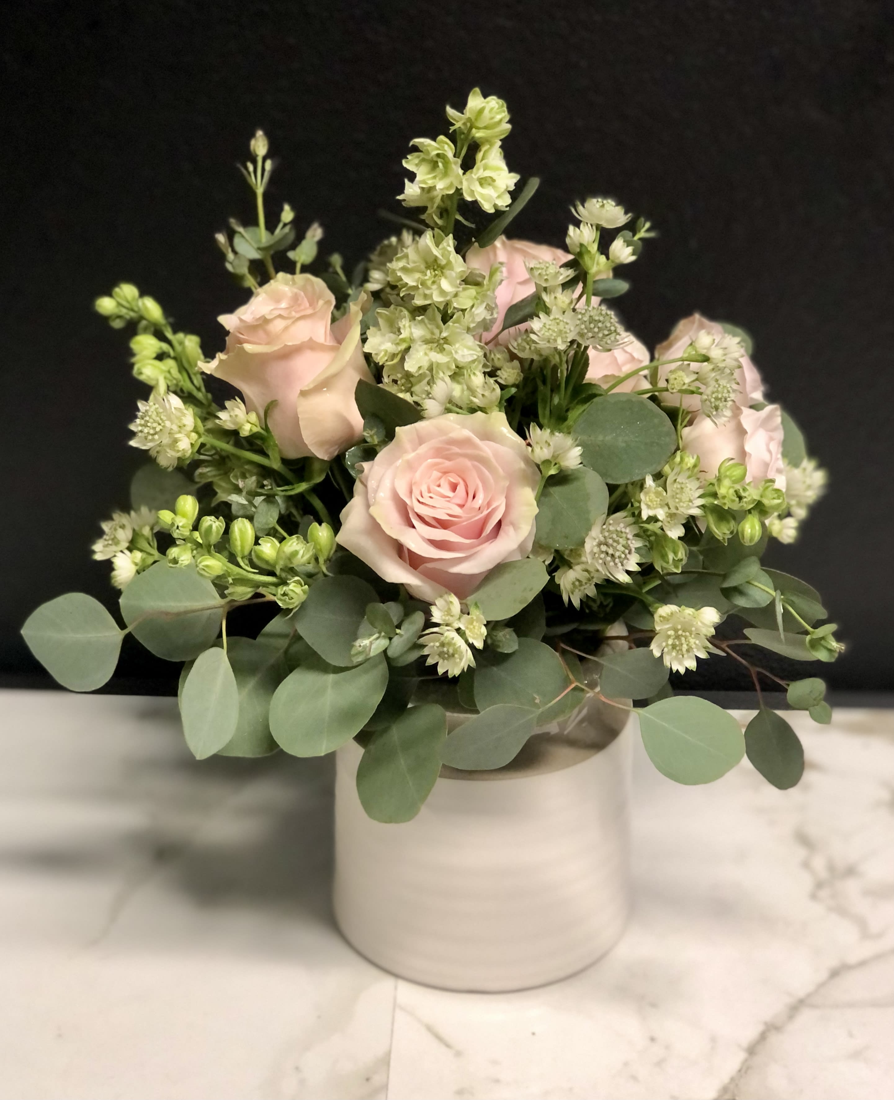 Blush roses and white filler flowers in a white vase