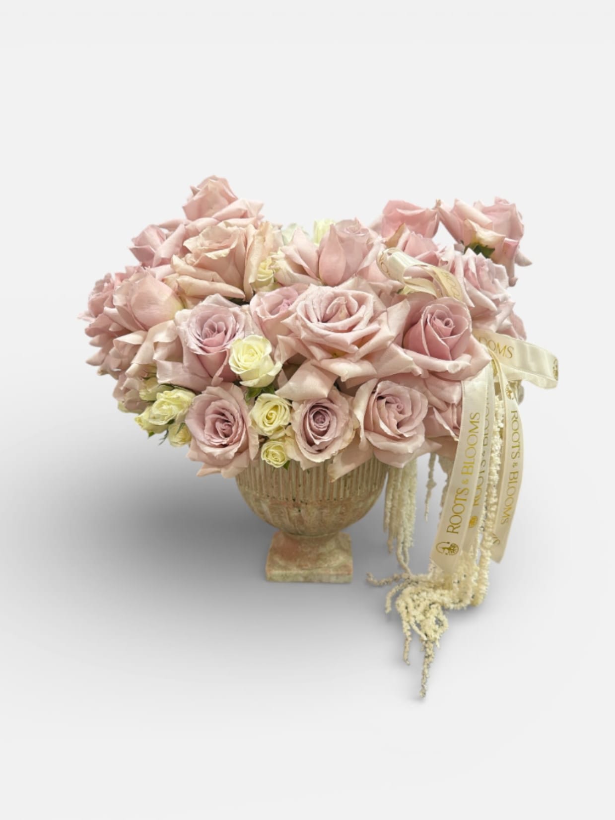 Blush pink roses arranged in a pedestal vase with a ribbon accent