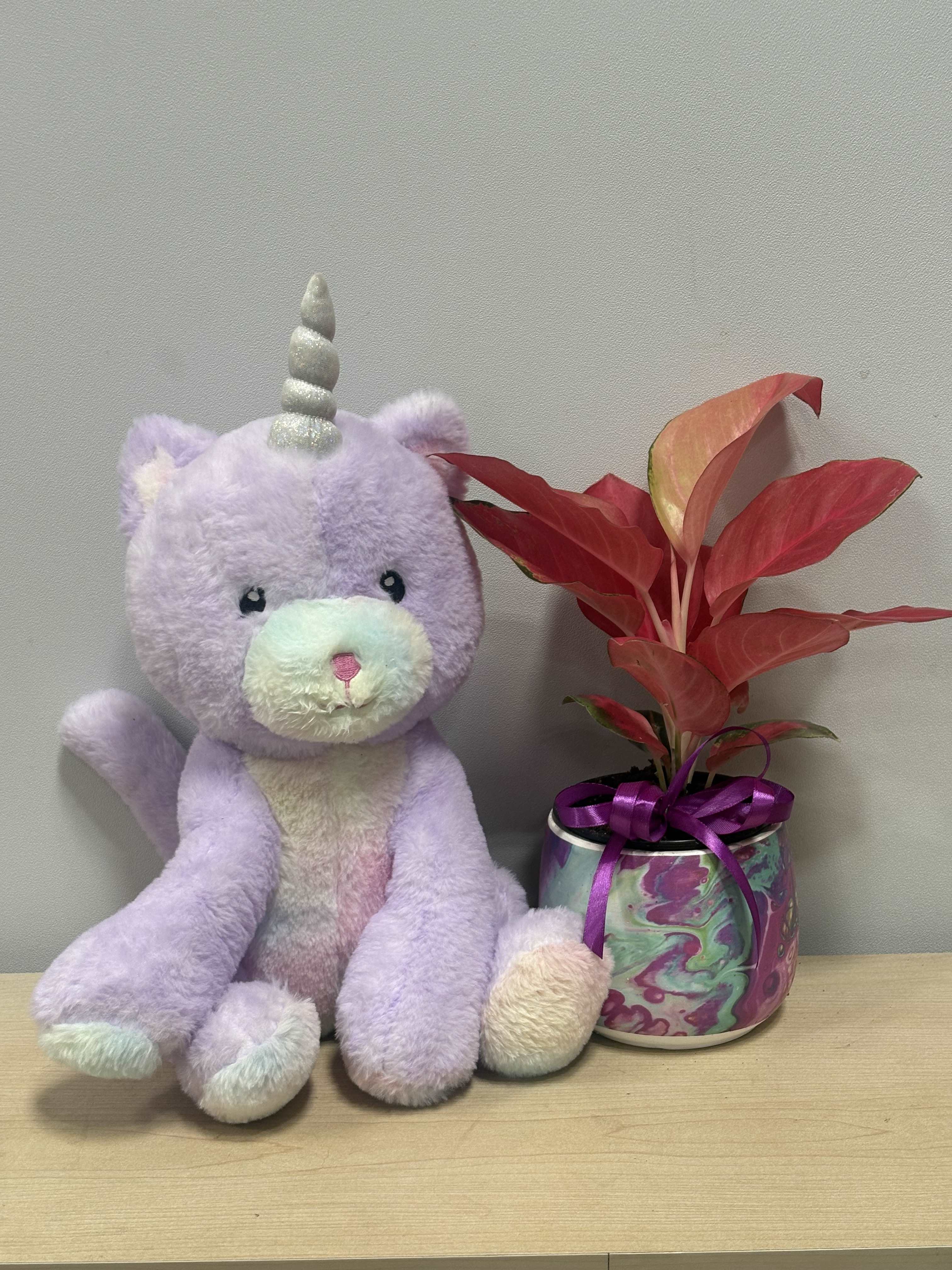 Plush unicorn beside a potted red-leaf plant in a decorative can