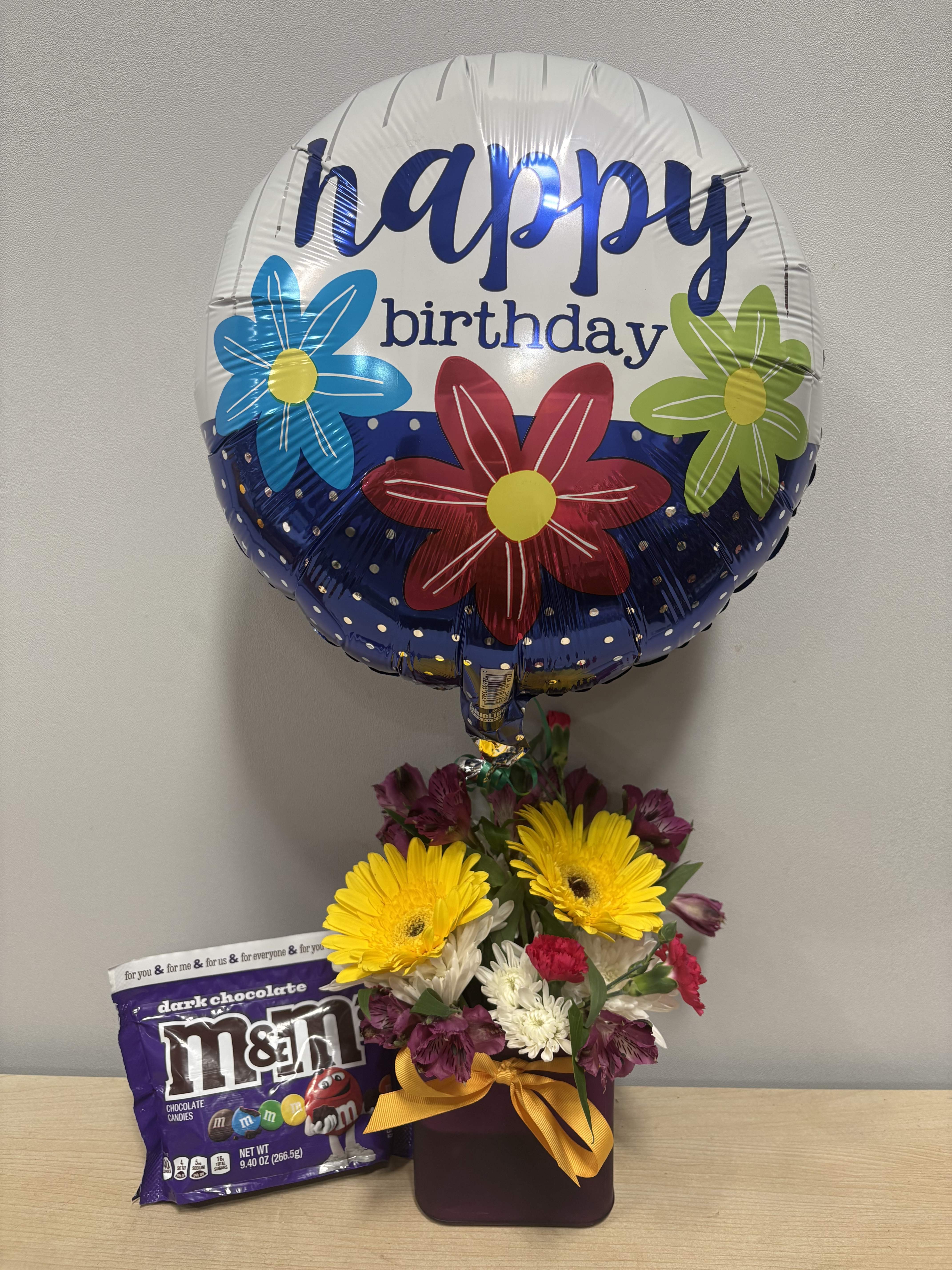 Birthday balloon with a mixed flower arrangement and a bag of M&amp;M's