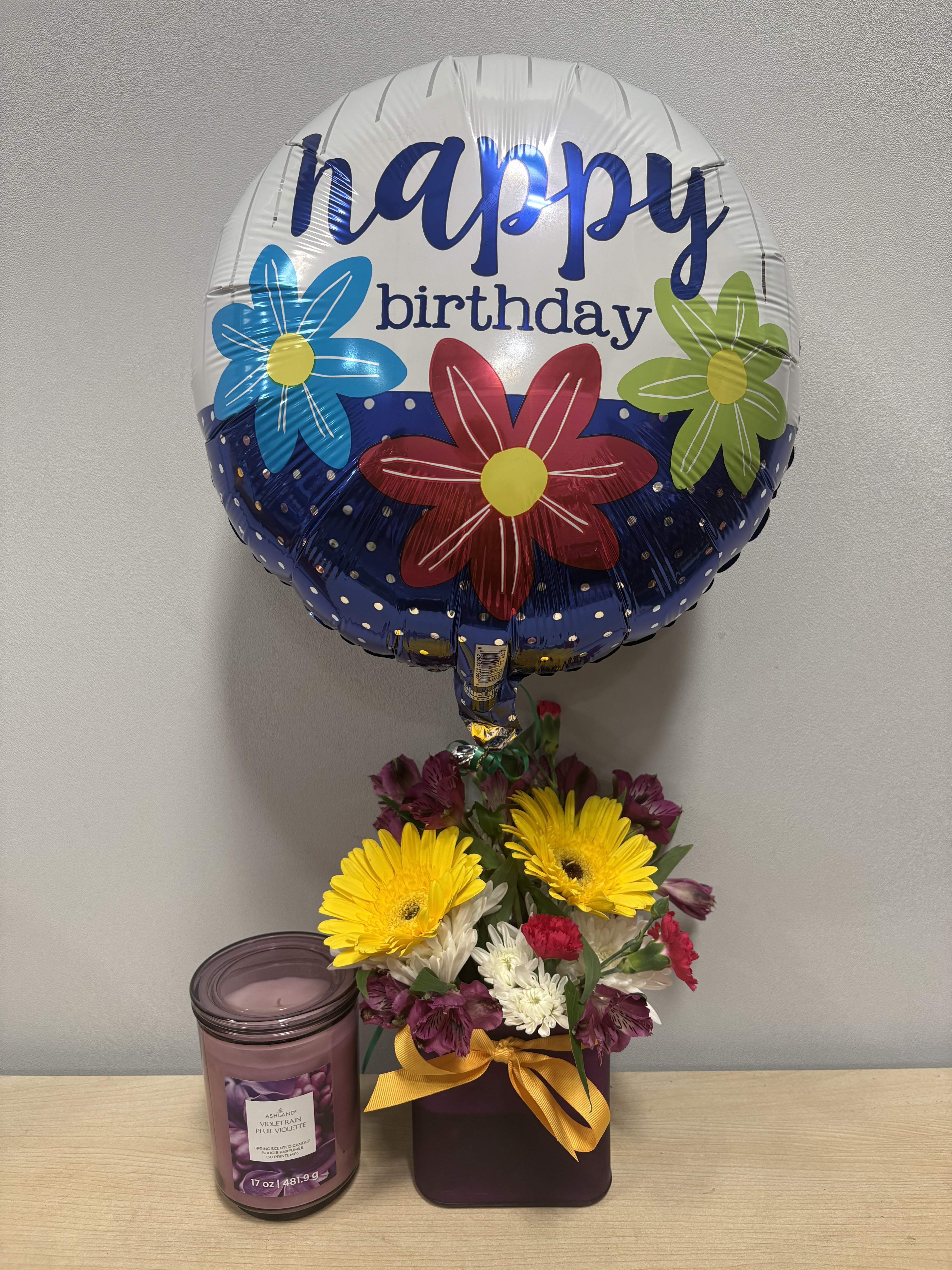 Birthday balloon above a mixed flower arrangement with a candle