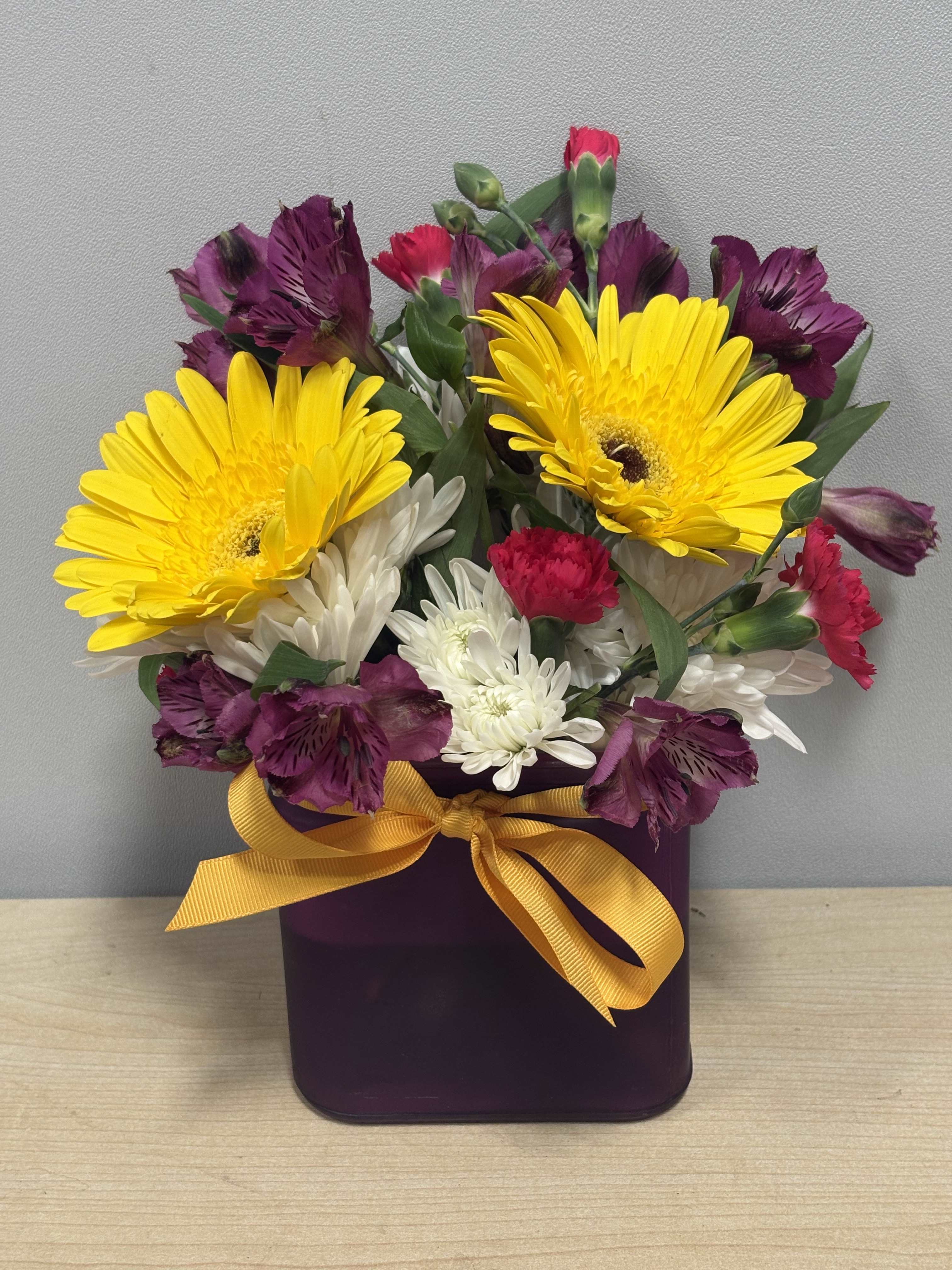 Bouquet of yellow gerbera daisies, white daisies, and purple alstroemeria in a purple box