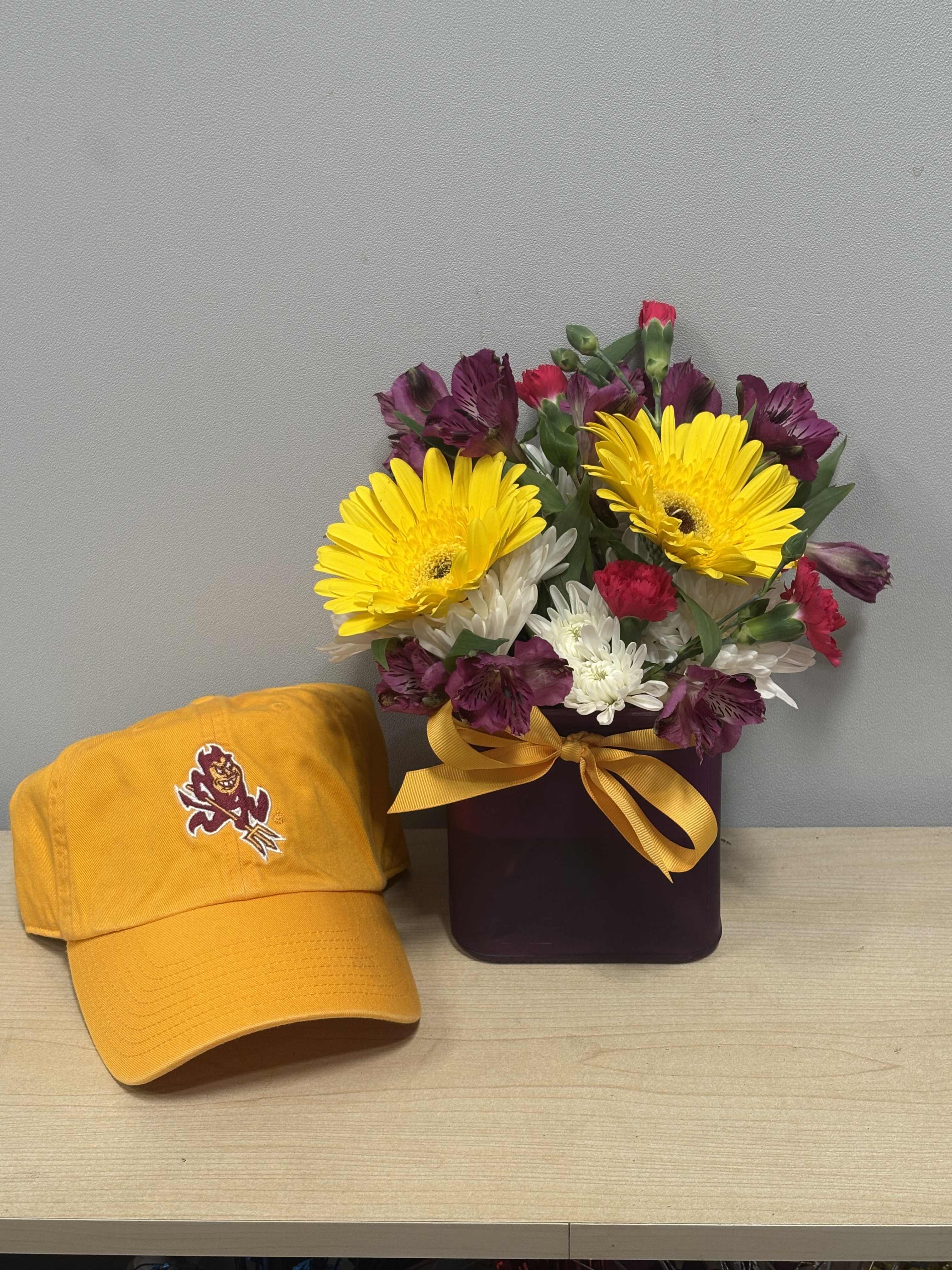 Mixed bouquet in a dark box with a yellow ribbon beside a yellow baseball cap