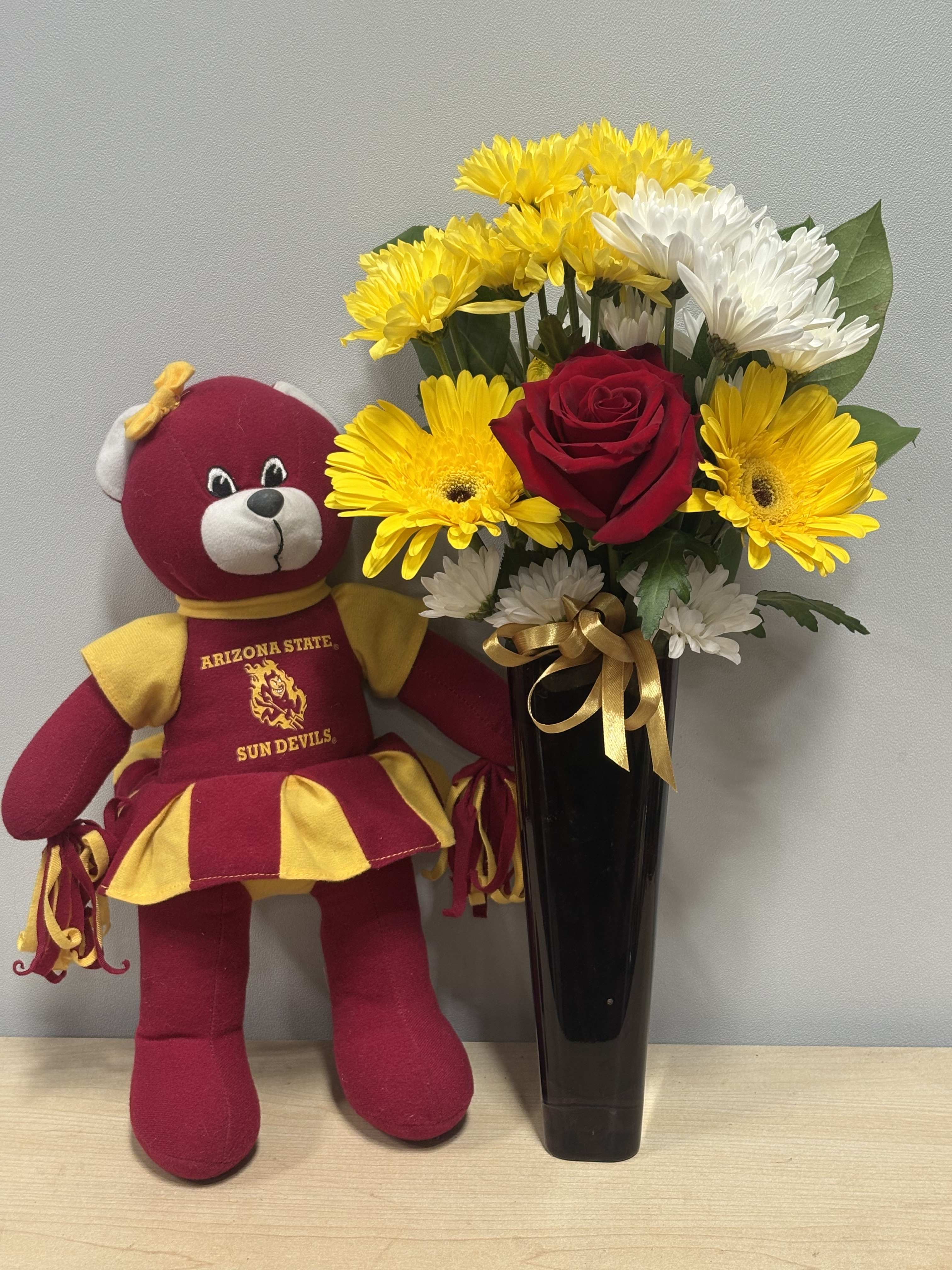 Bouquet of yellow and white daisies with a red rose in a black vase beside a teddy bear