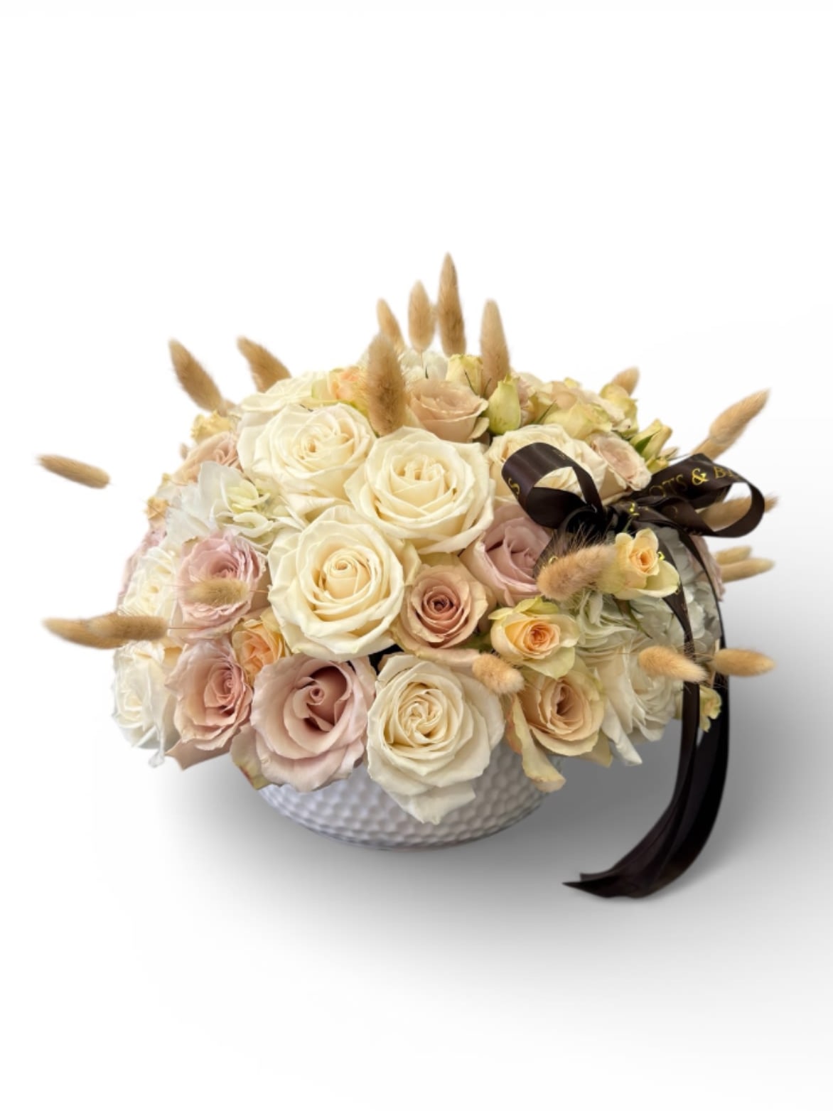 Cream and blush roses in a white textured bowl with a dark ribbon