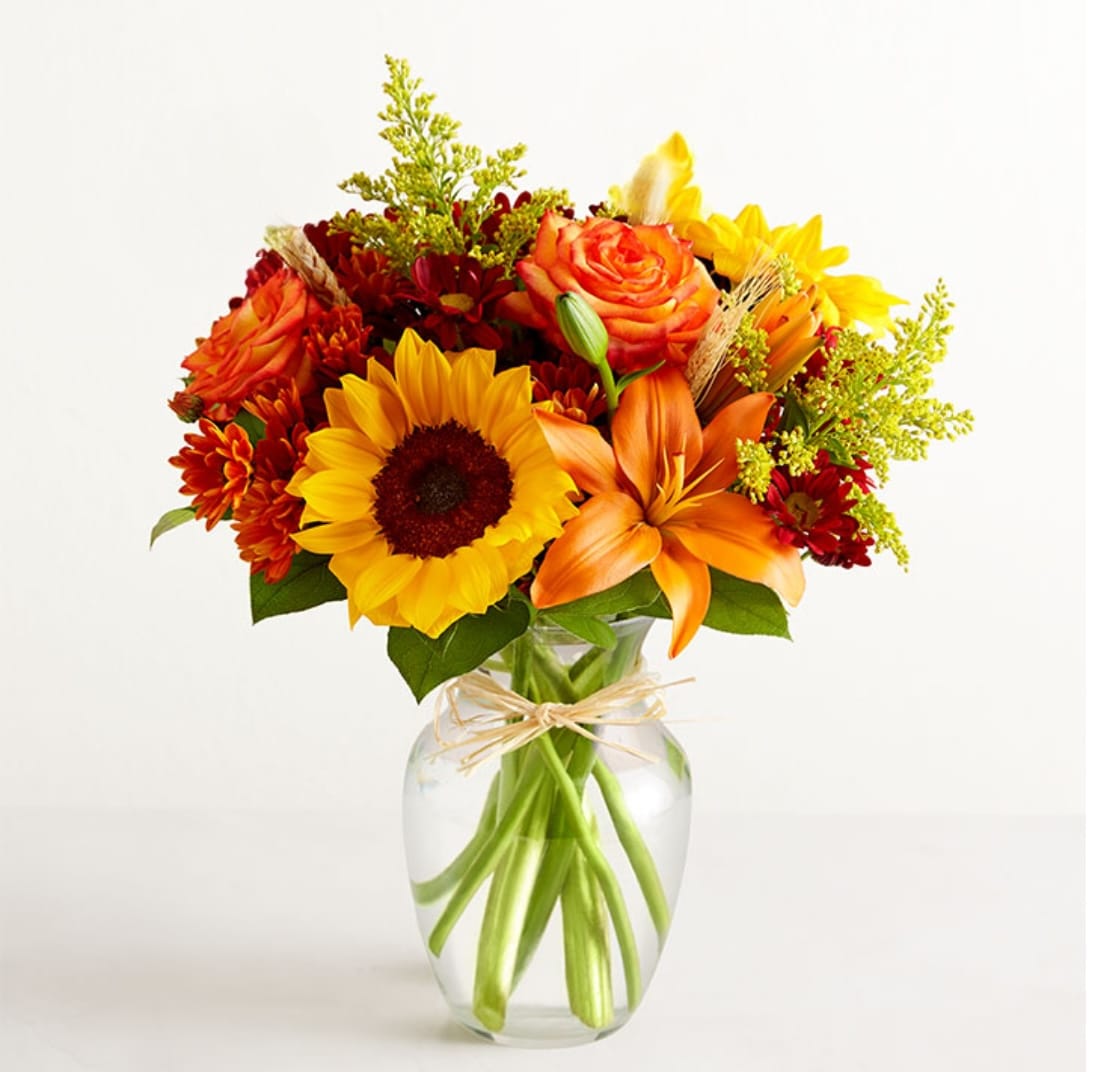 Bouquet of sunflowers, orange roses, and lilies in a clear glass vase